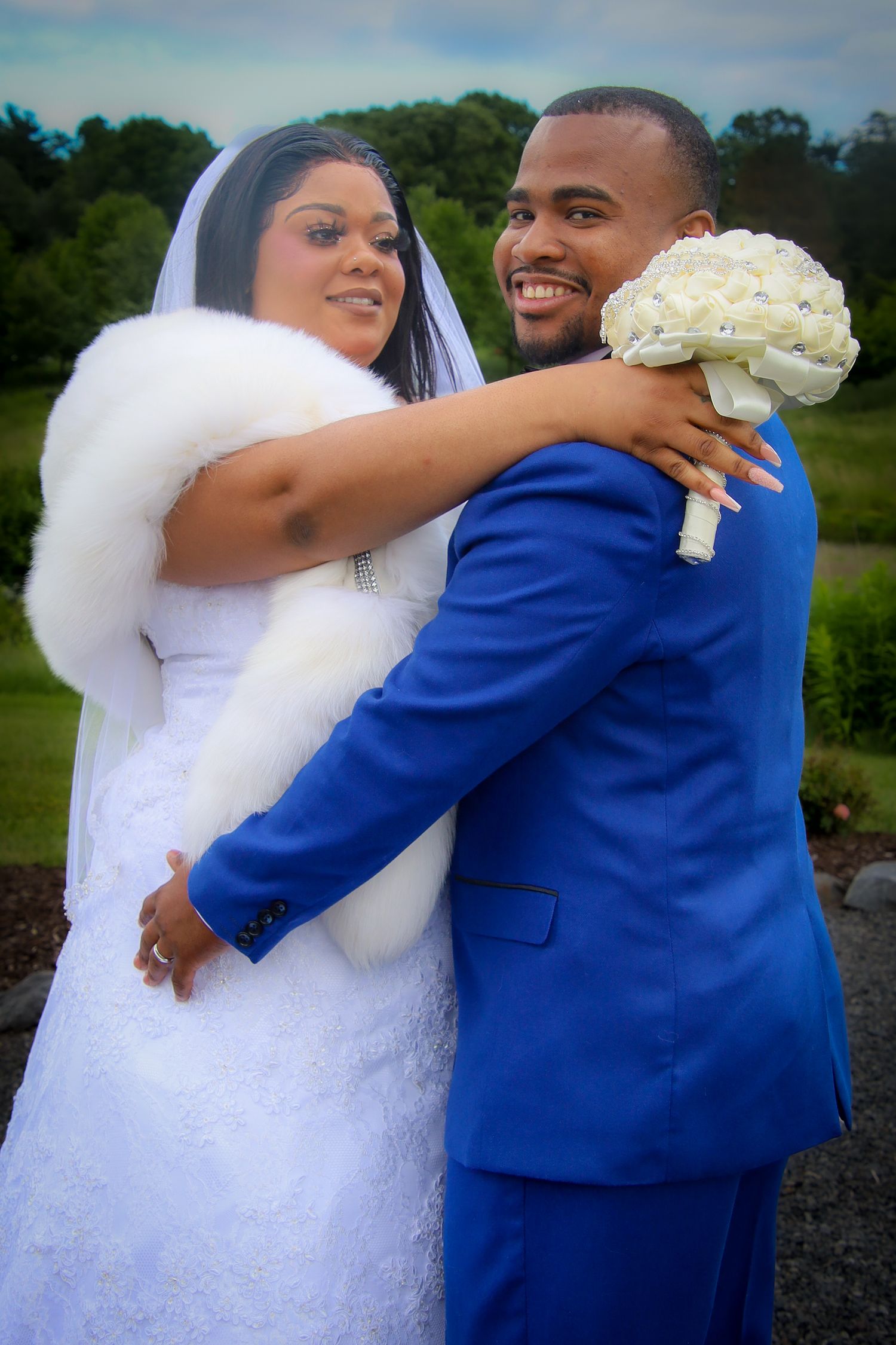 A couple in wedding attire embraces outdoors, with the bride in white and groom in royal blue sharing tender moments.