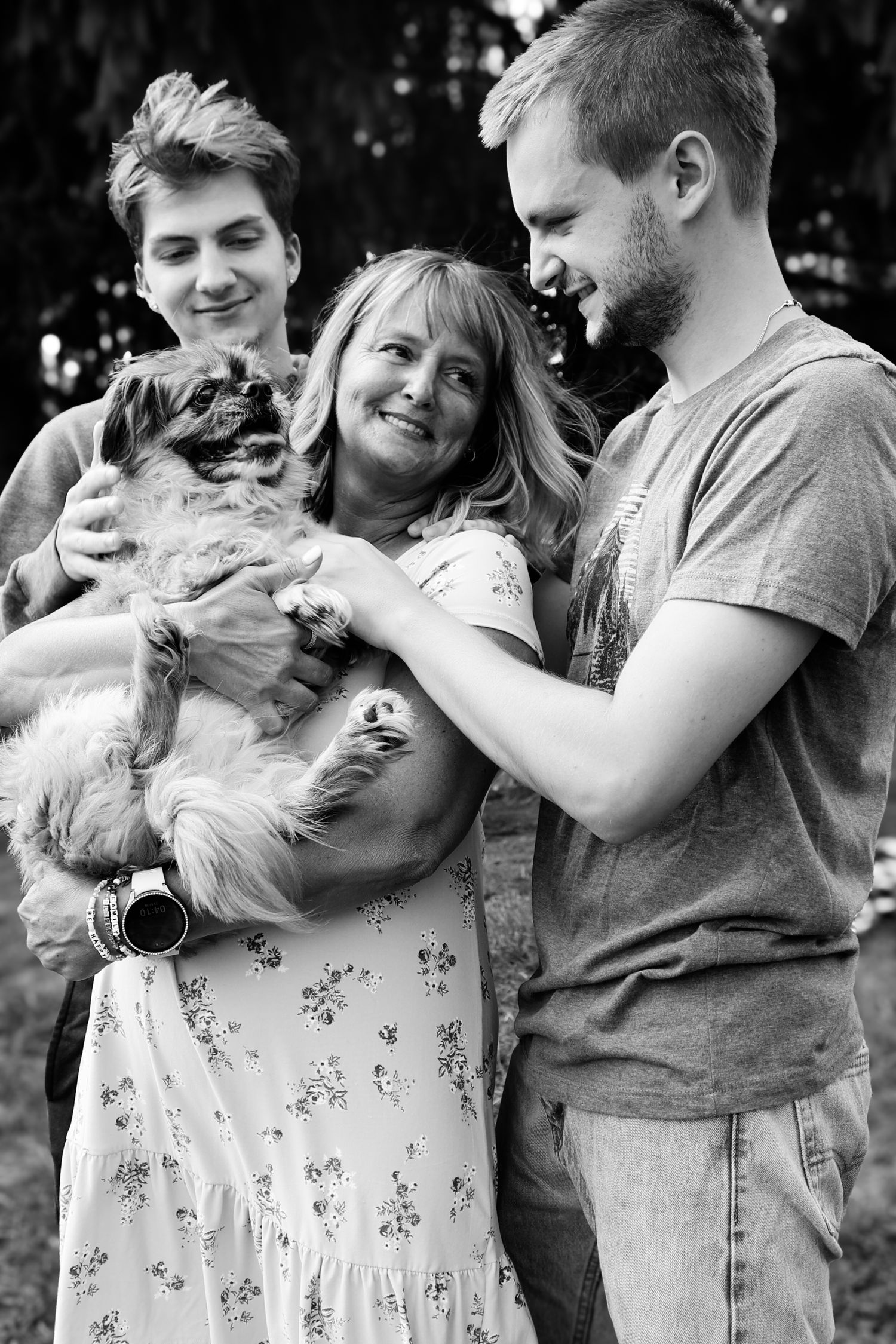A couple in casual attire shares playful moments with their small white dog in a series of black and white photos.