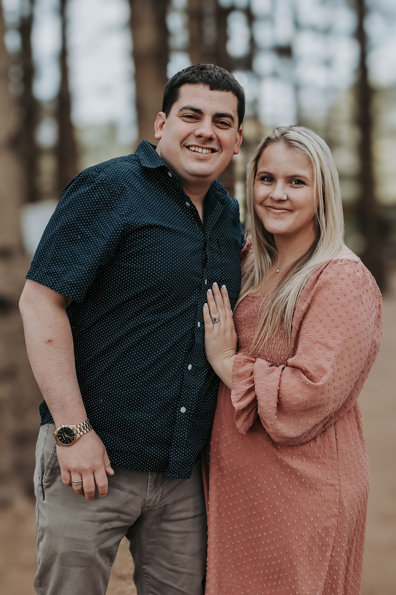 A couple in coordinating outfits share romantic moments in a wooded outdoor setting during a photo session.