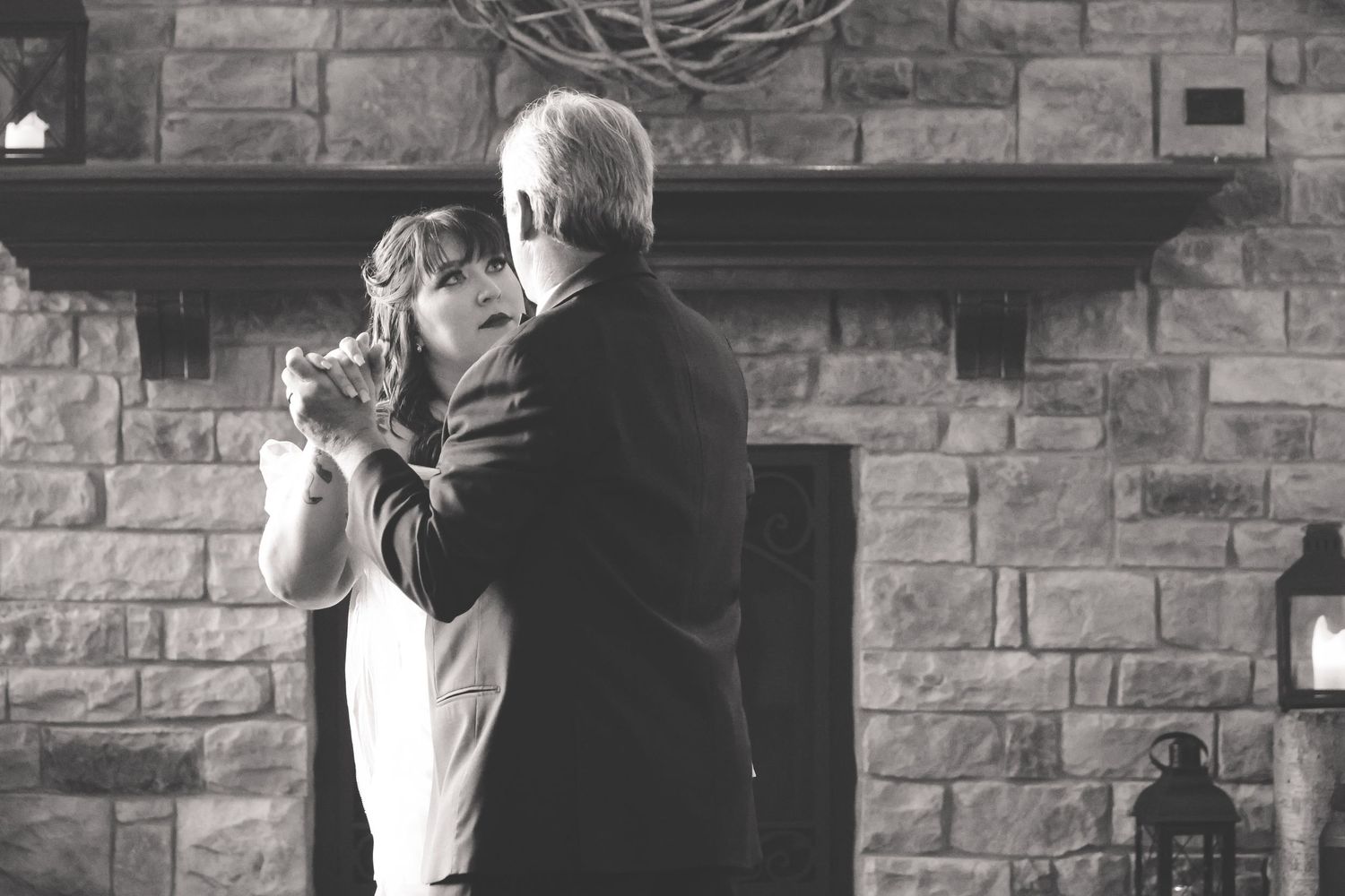 Four black and white photos showing a couple embracing and dancing together in front of a stone wall.