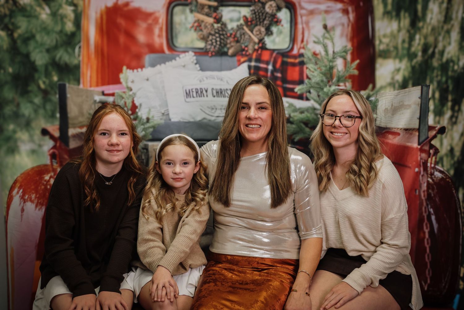 A group sits together on a red vintage truck decorated for Christmas with plaid bows and greenery.