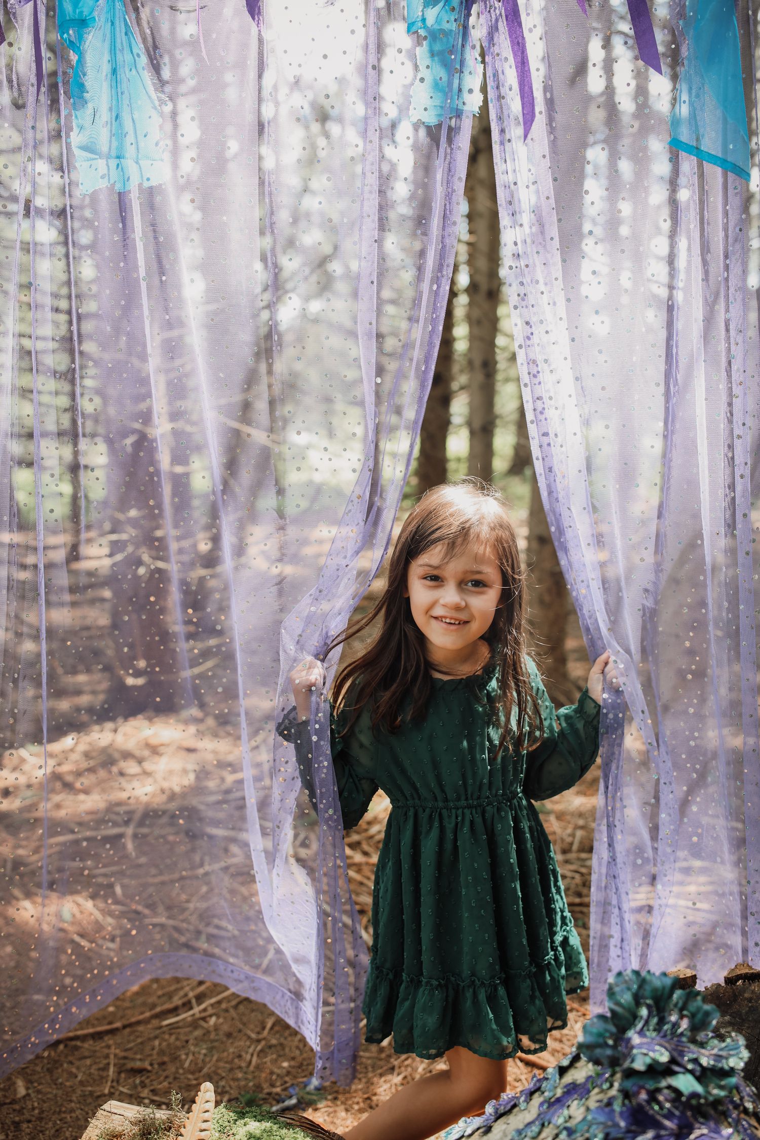 Whimsical forest scene with sparkly purple and blue tulle fabric hanging from trees creating a magical atmosphere.