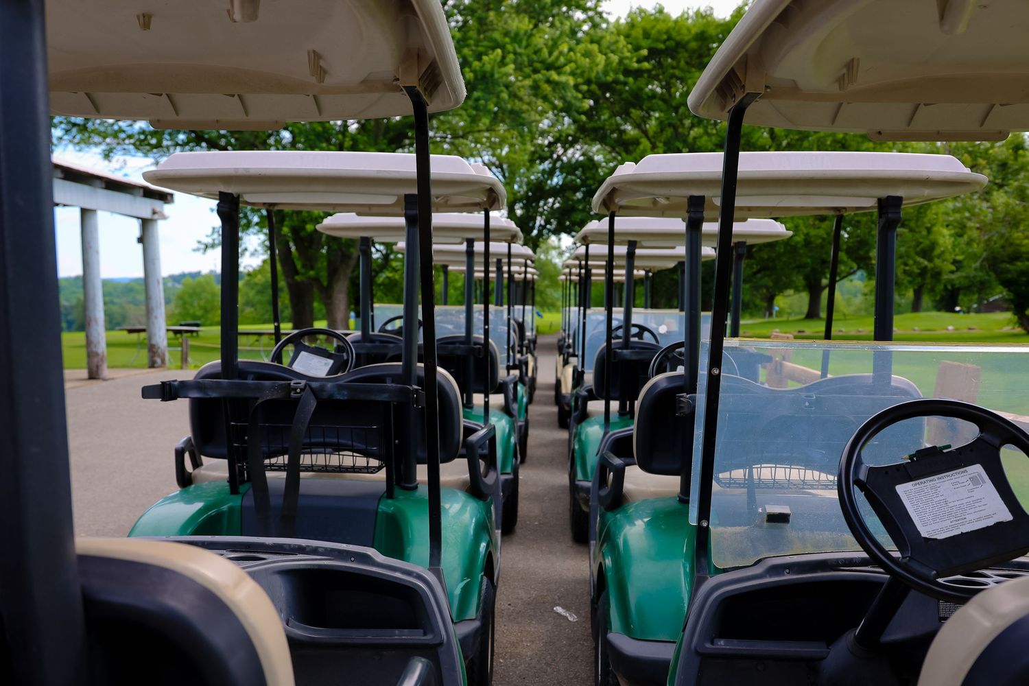 Row of golf carts with turquoise seats parked under covered shelter at golf course.