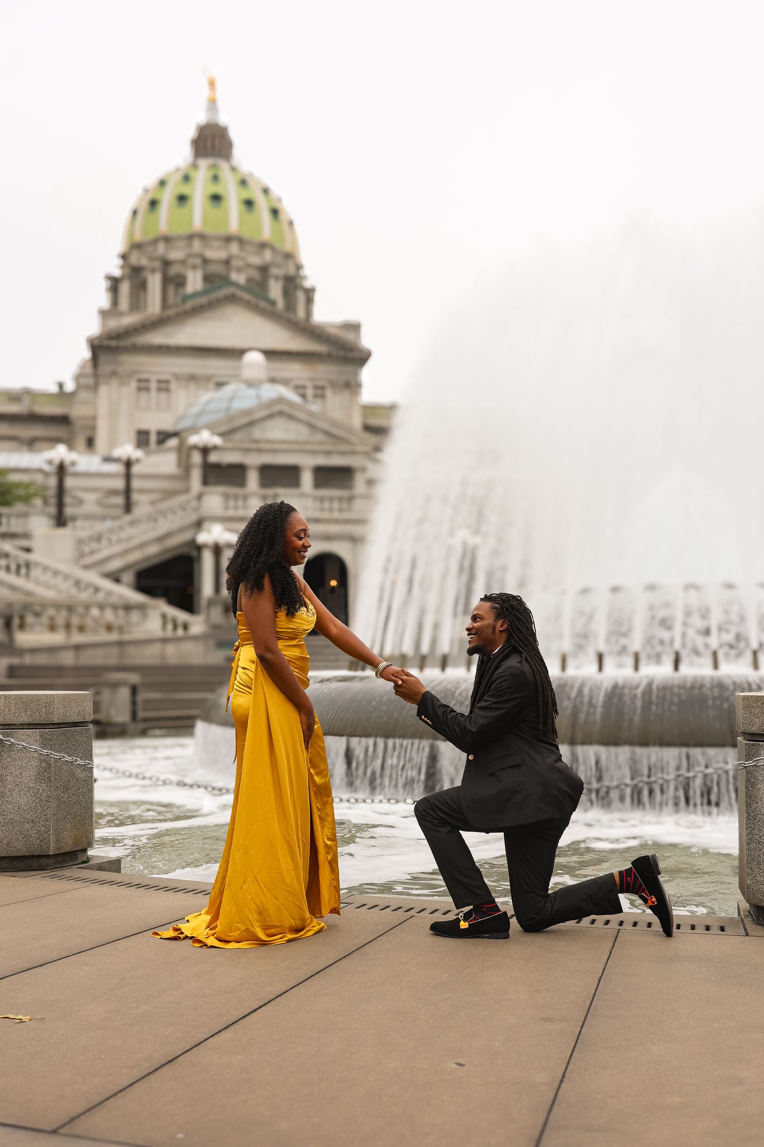 A romantic marriage proposal sequence in front of a grand domed building with fountains in the background.