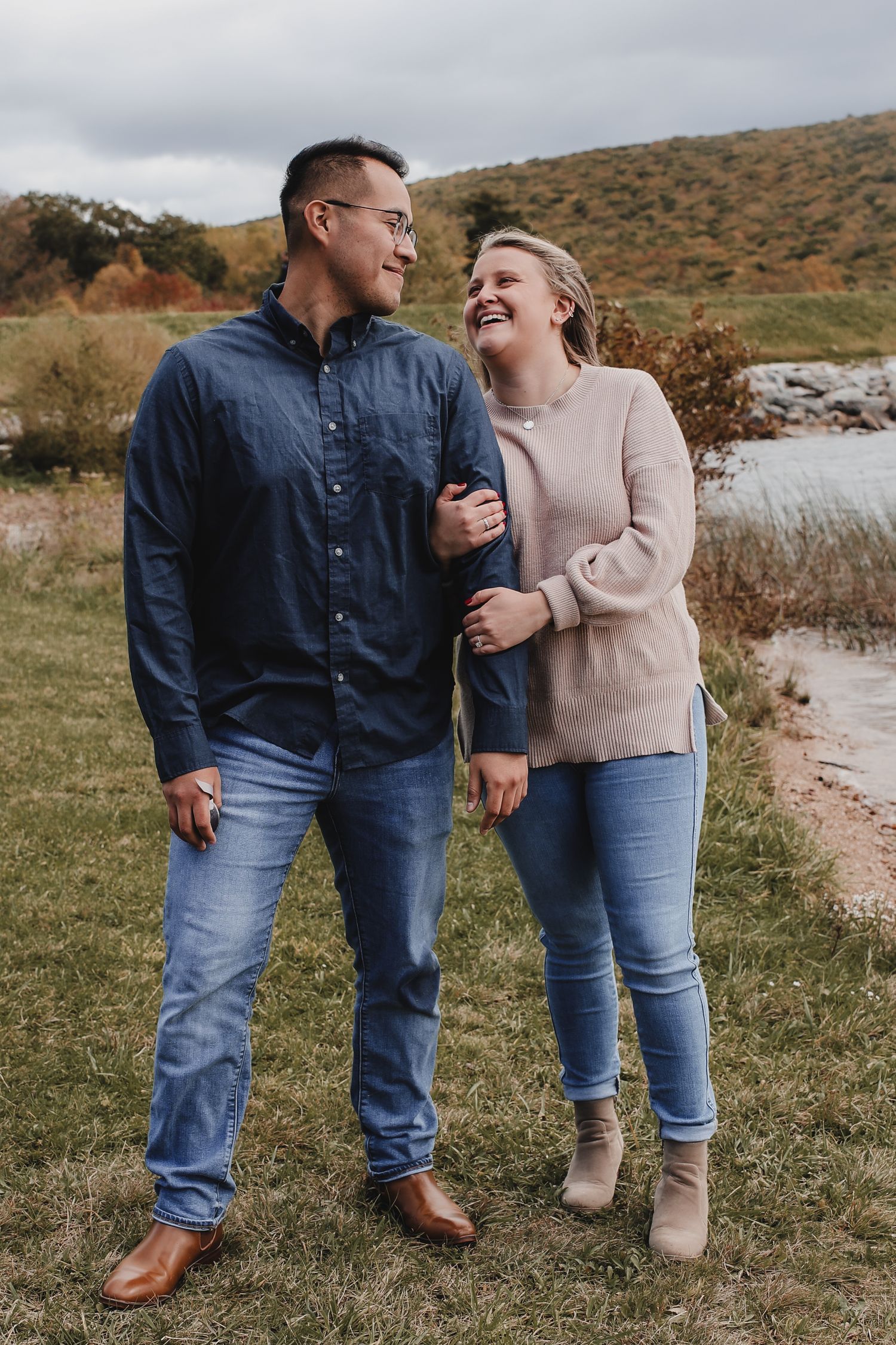 A couple shares a joyful moment together outdoors on a grassy path with hills in the background.