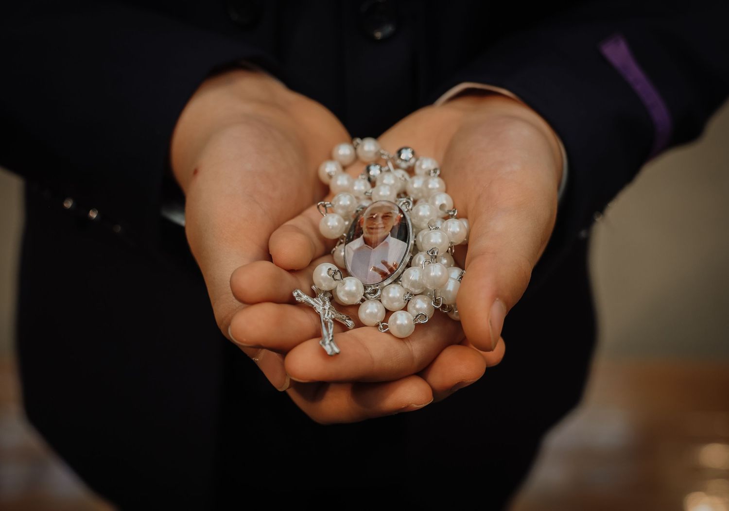 Hands gently hold a collection of delicate pearl beads against a dark background.