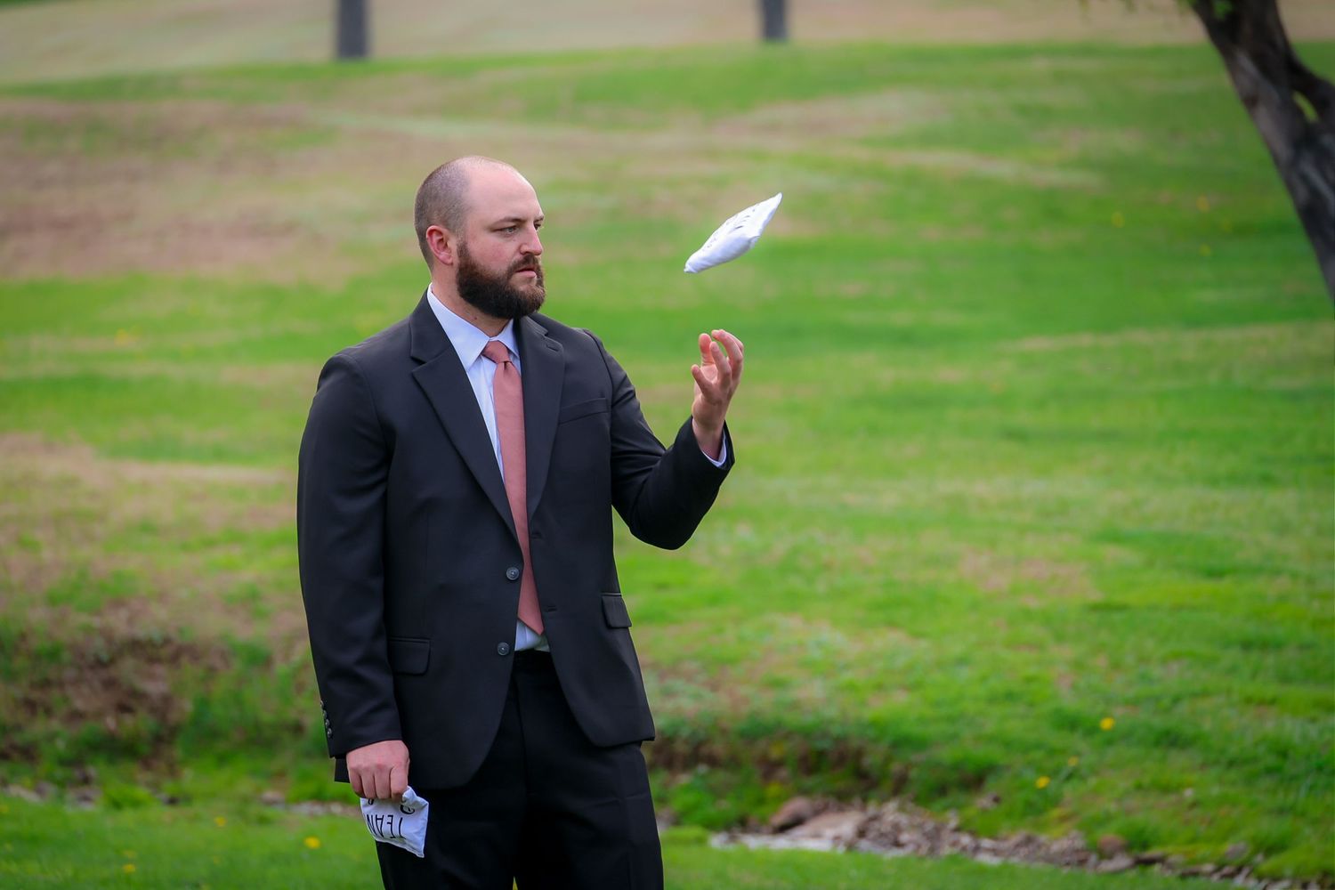 Man in suit tossing paper airplane on green grass field outdoors.