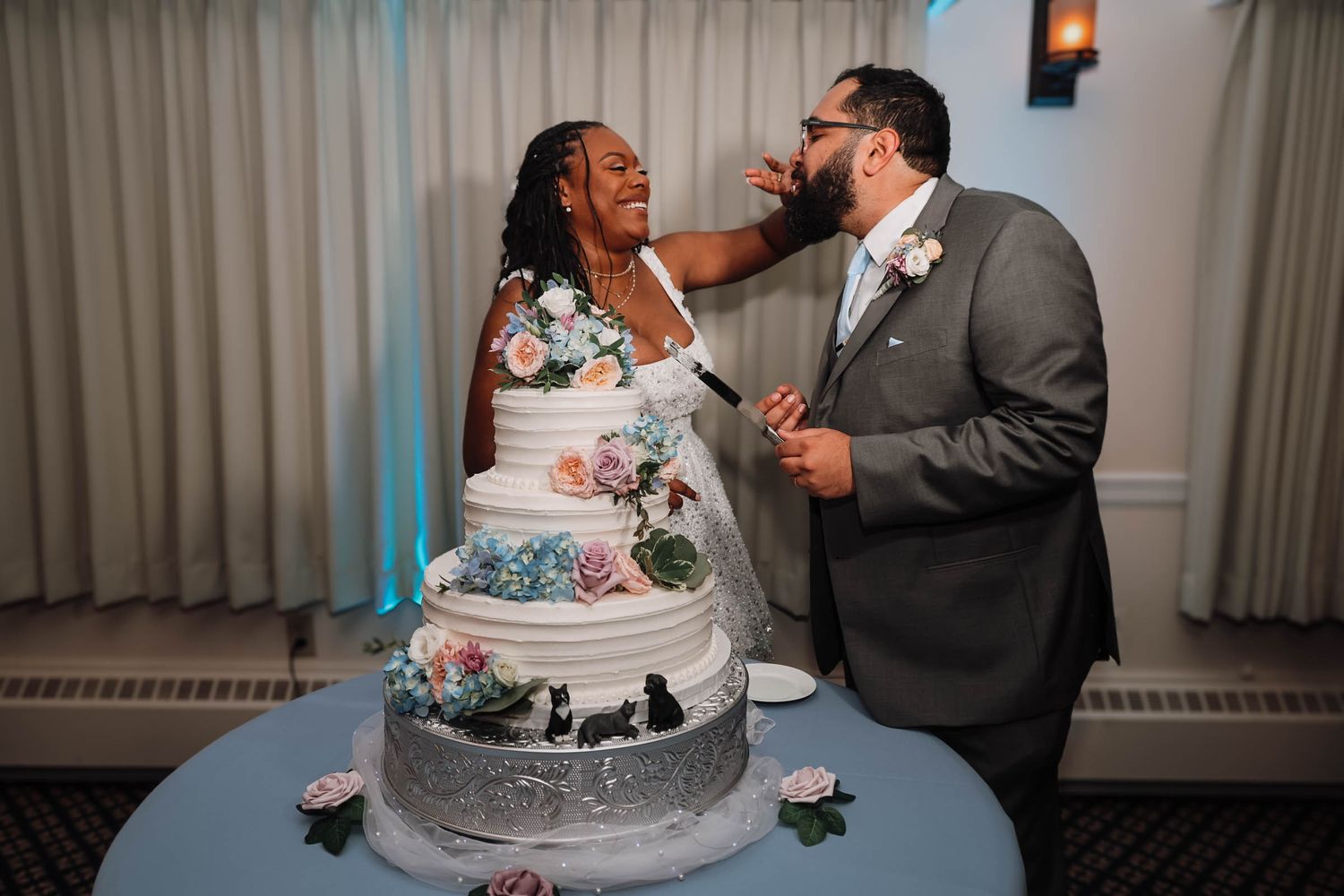 Bride smearing wedding cake on groom's face during fun cake cutting ceremony at elegant wedding reception.