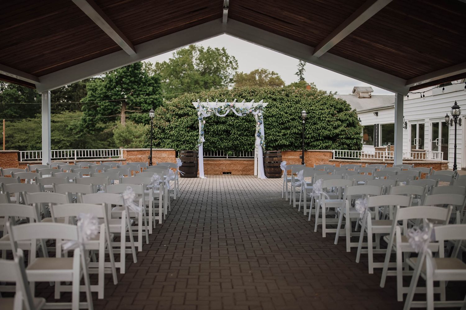 Elegant outdoor wedding ceremony setup with white chairs, floral arch, and lush greenery at a classic venue.