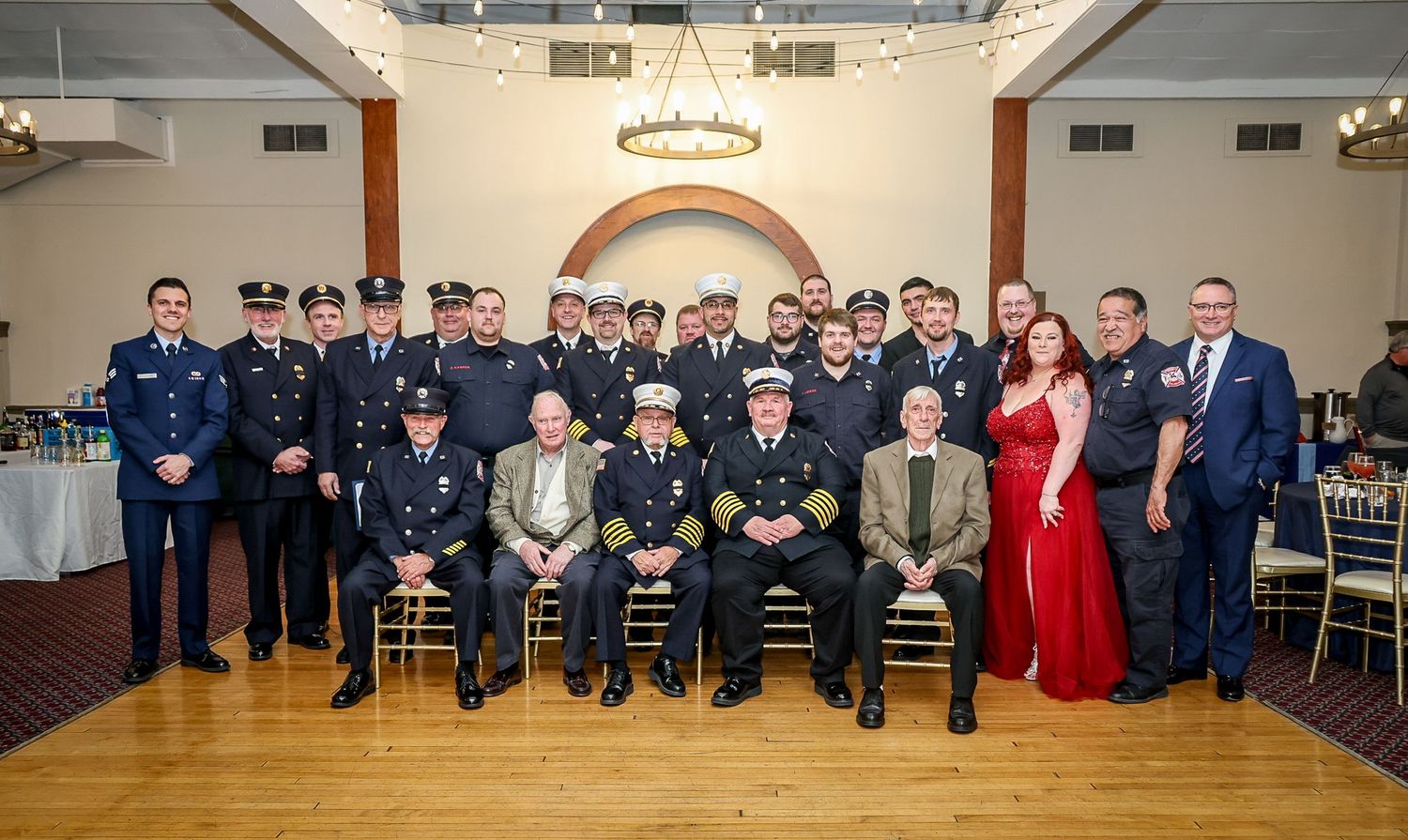 Group photo of firefighters and officials in dress uniforms at a formal banquet hall ceremony.