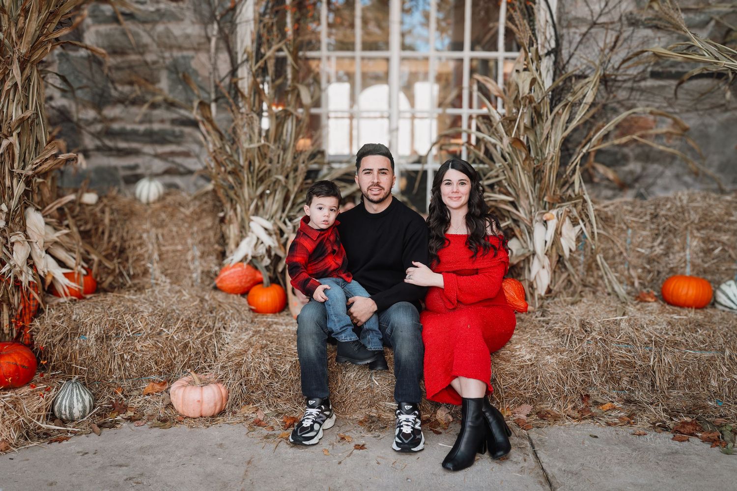 A couple poses for autumn photos among pumpkins and stone walls in a seasonal outdoor setting.