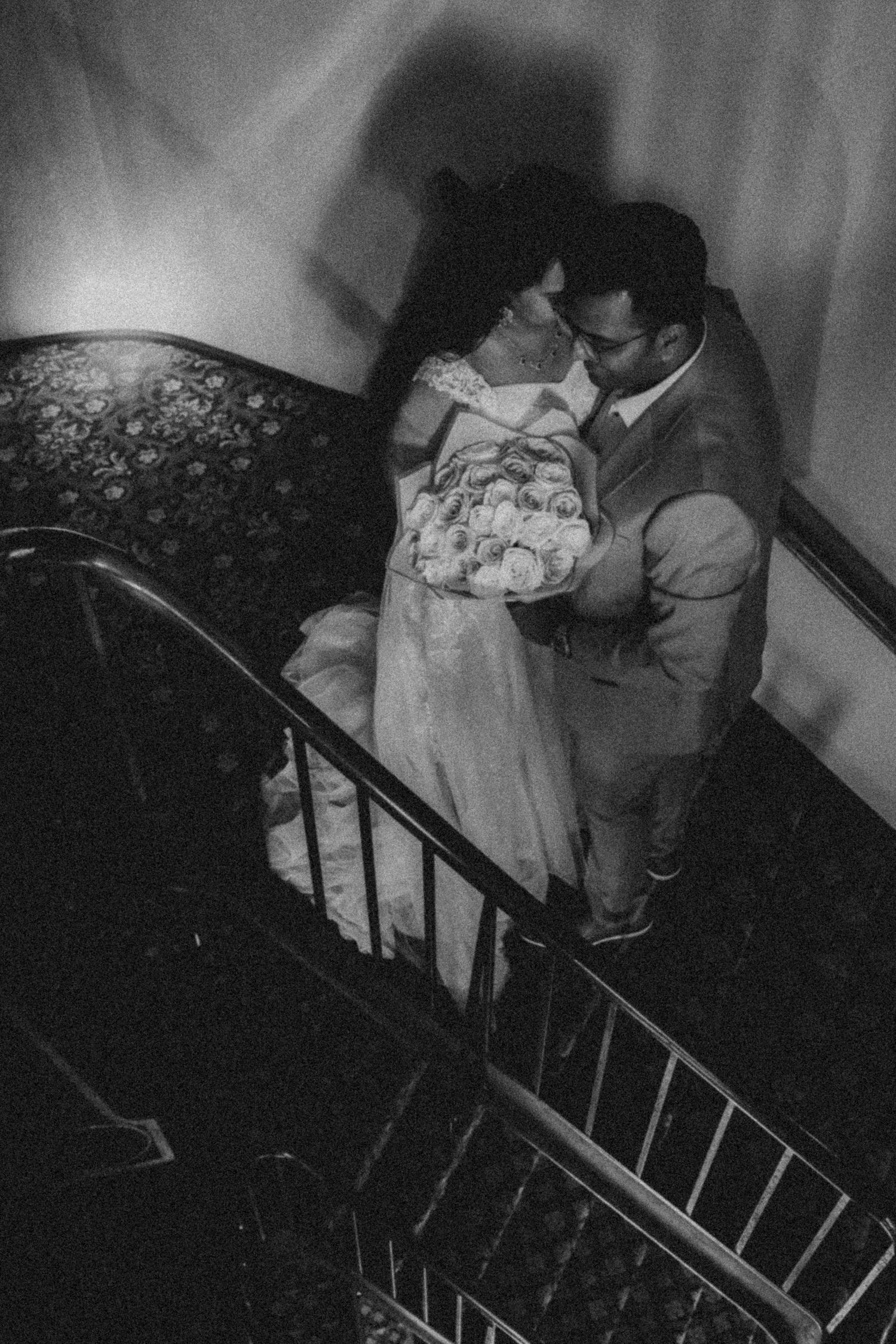 A haunting black and white photograph shows figures descending a dimly lit staircase in what appears to be a vintage setting.