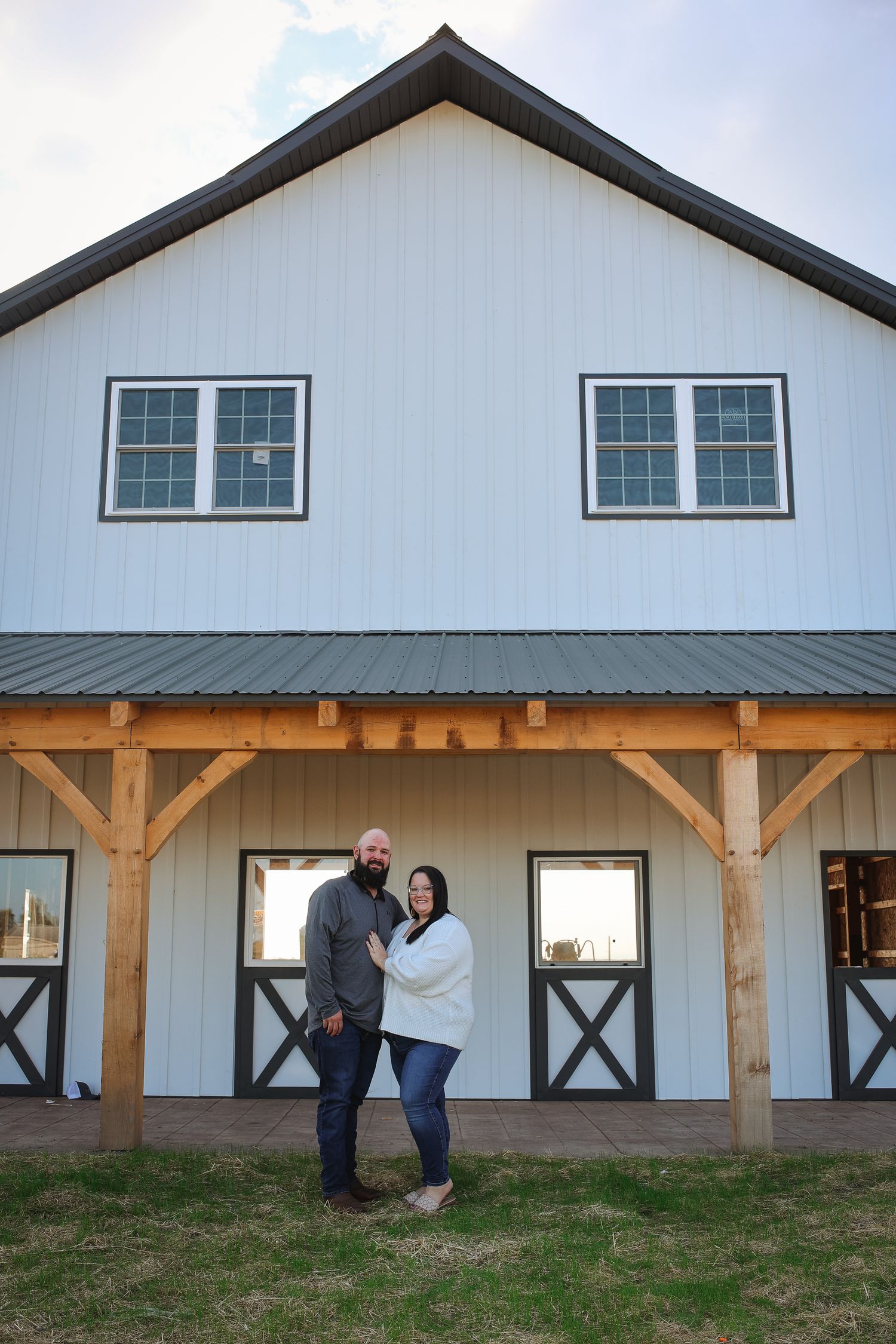 Long white barn-style building with wooden posts and black trim features multiple windows and a sloped roof.