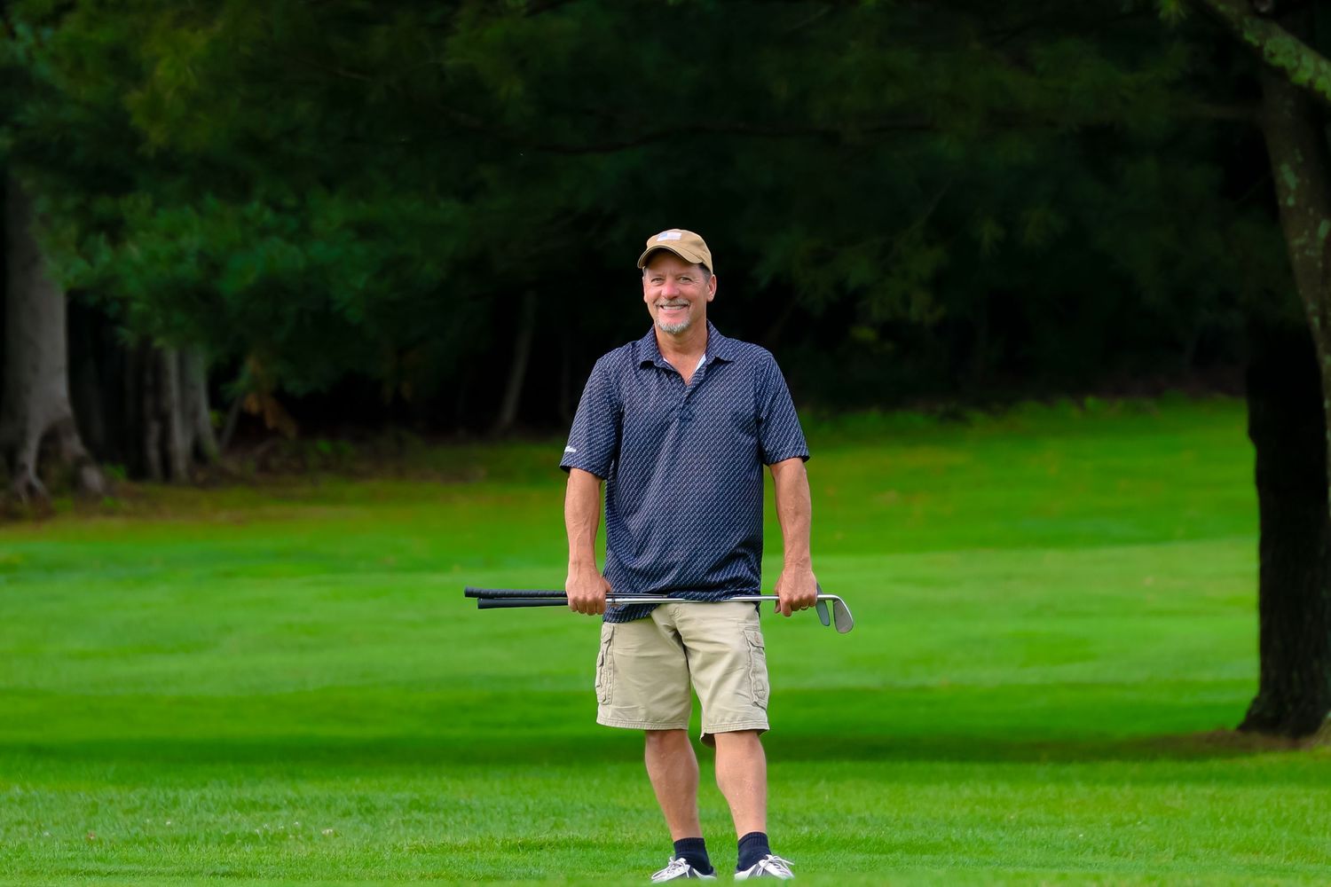 A golfer in blue stands on a lush green course with trees in the background, preparing to take a shot.