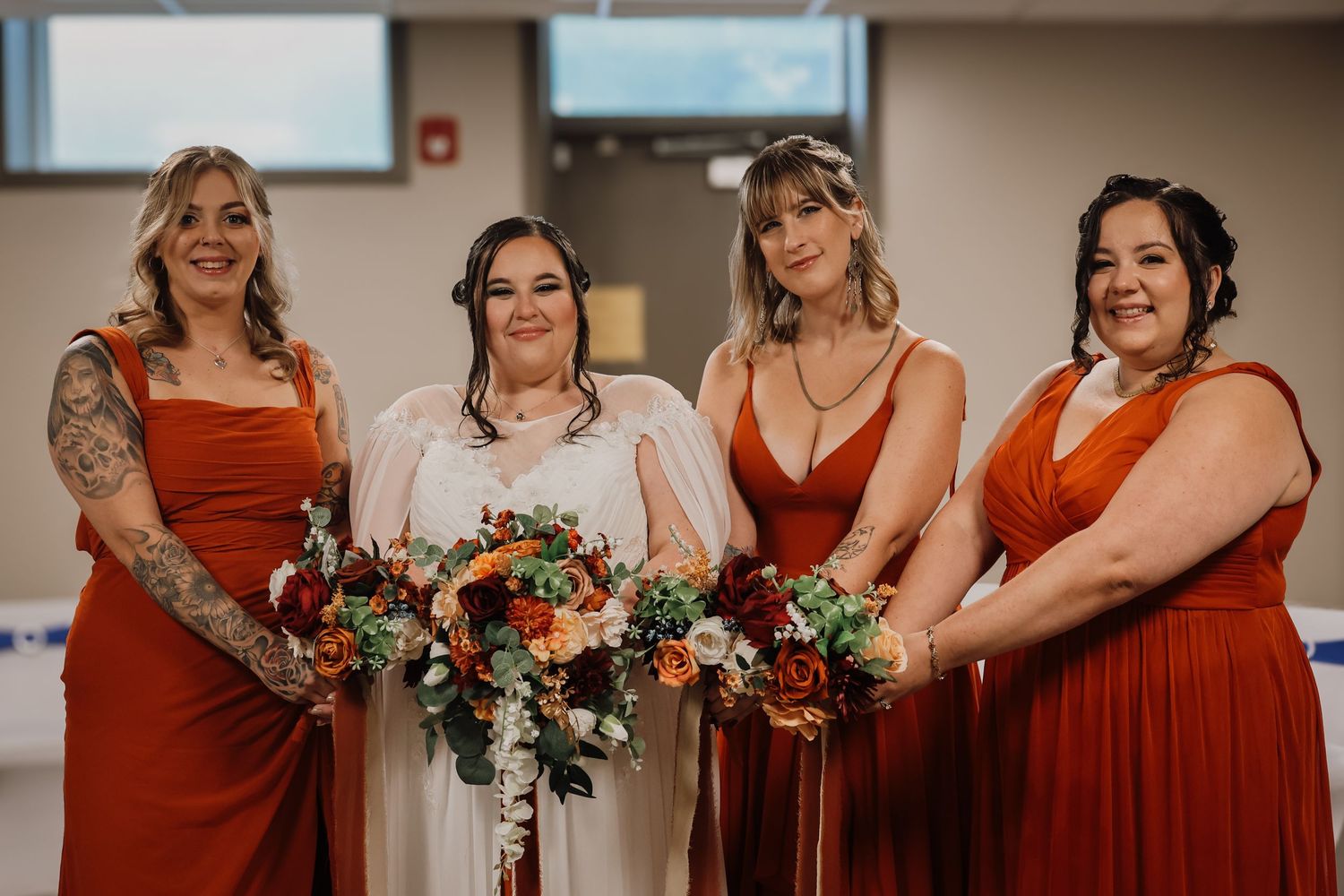 A group wearing matching rust-colored bridesmaid dresses pose together at a wedding celebration.