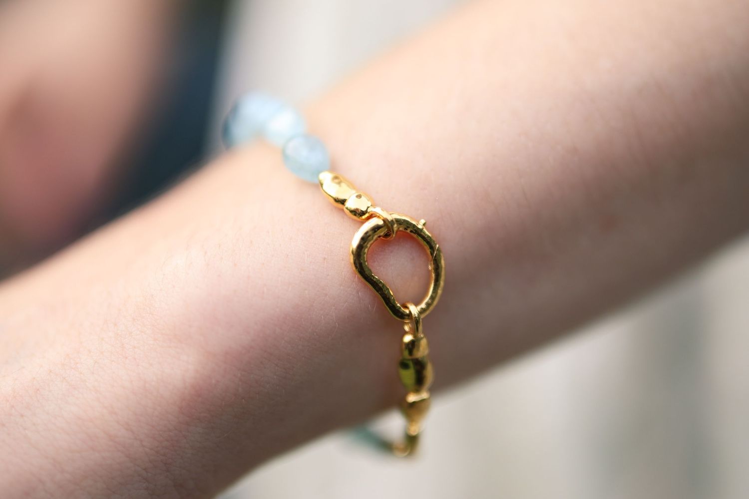 Close-up detail of delicate gold jewelry pieces laid out on a soft pink surface.
