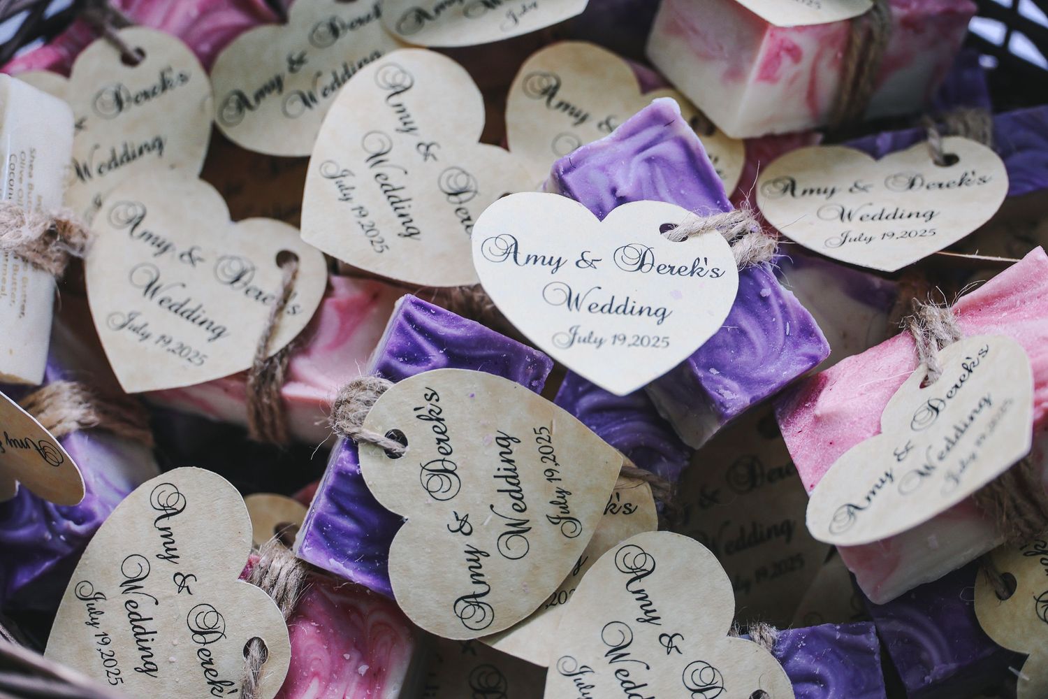 Heart-shaped wedding favor tags with handwritten text arranged on a surface with pink and purple ribbons.