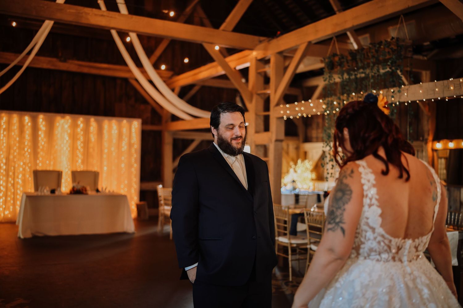 A romantic wedding dance between a couple in a rustic barn venue with warm lighting and decorative string lights overhead.