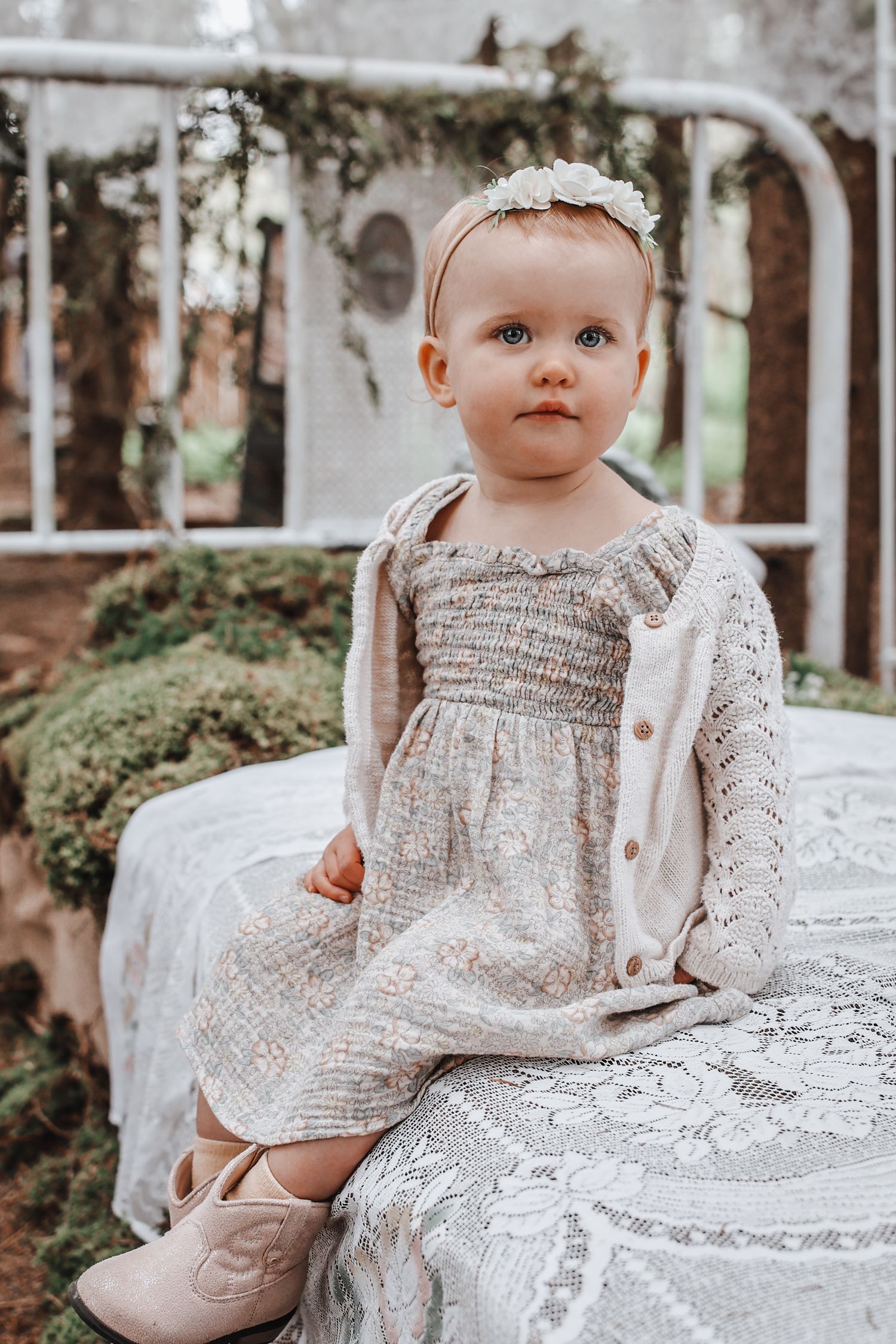 Baby in vintage lace dress posed on white antique furniture outdoors.