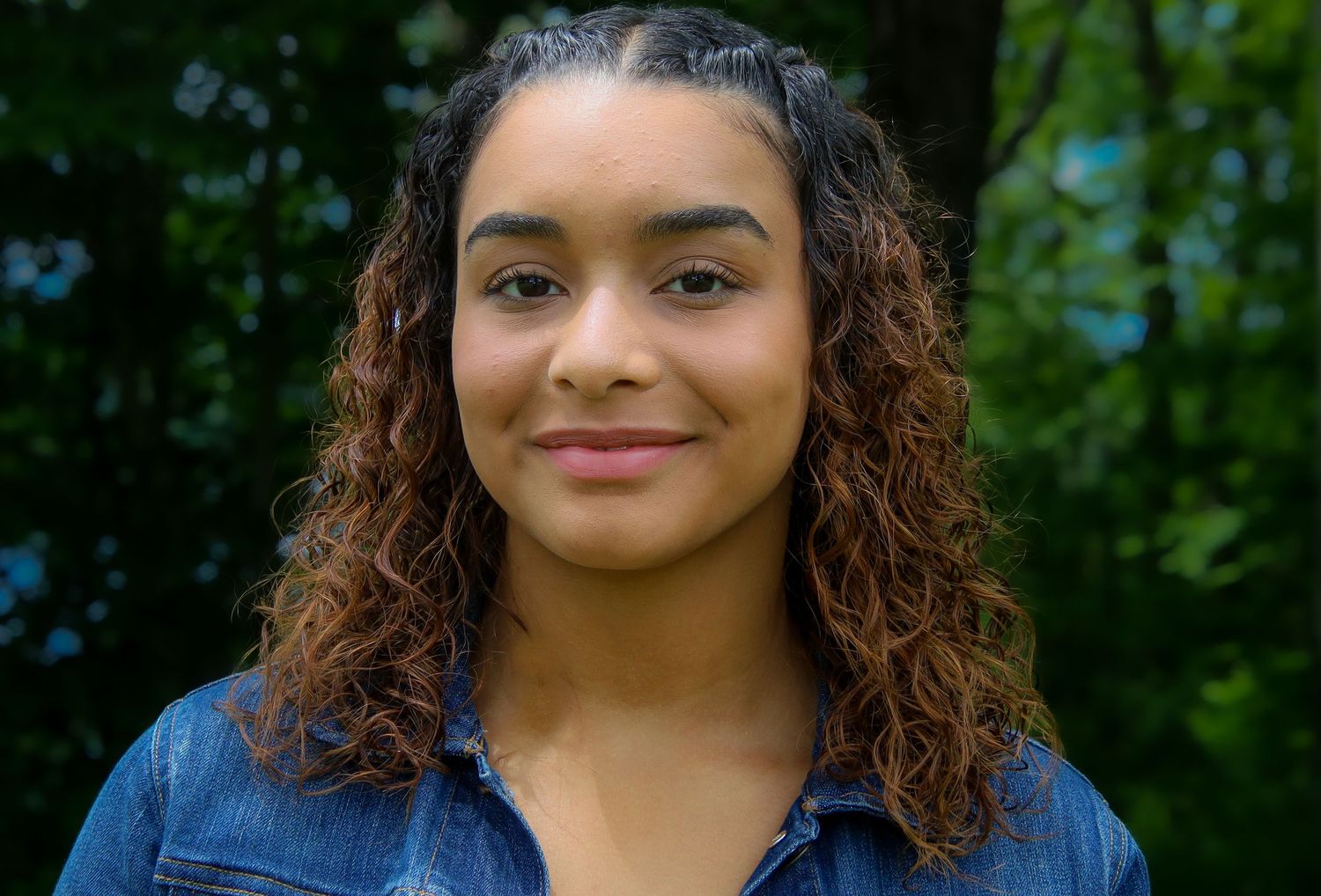 A series of four close-up portraits of a person with curly hair against a lush green outdoor background.