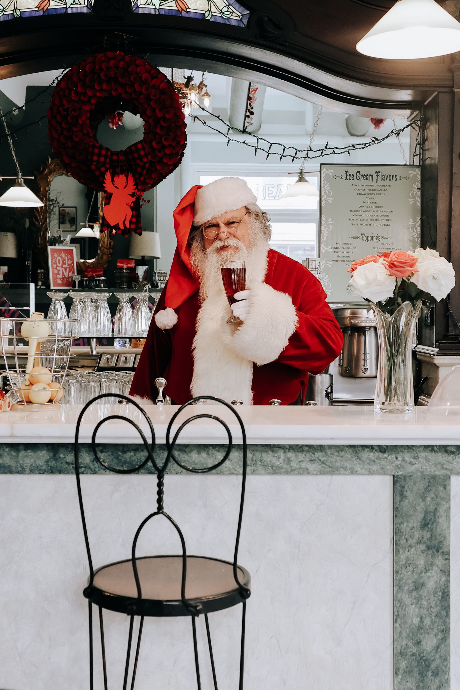 A festive holiday scene with Santa Claus and Christmas decorations including red wreaths and white pendant lights.