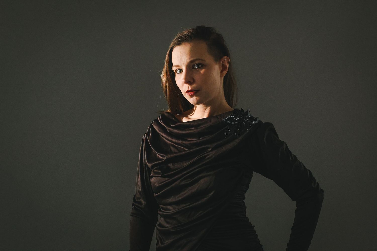 Young woman in a dark draped top posing confidently against a gray studio background.