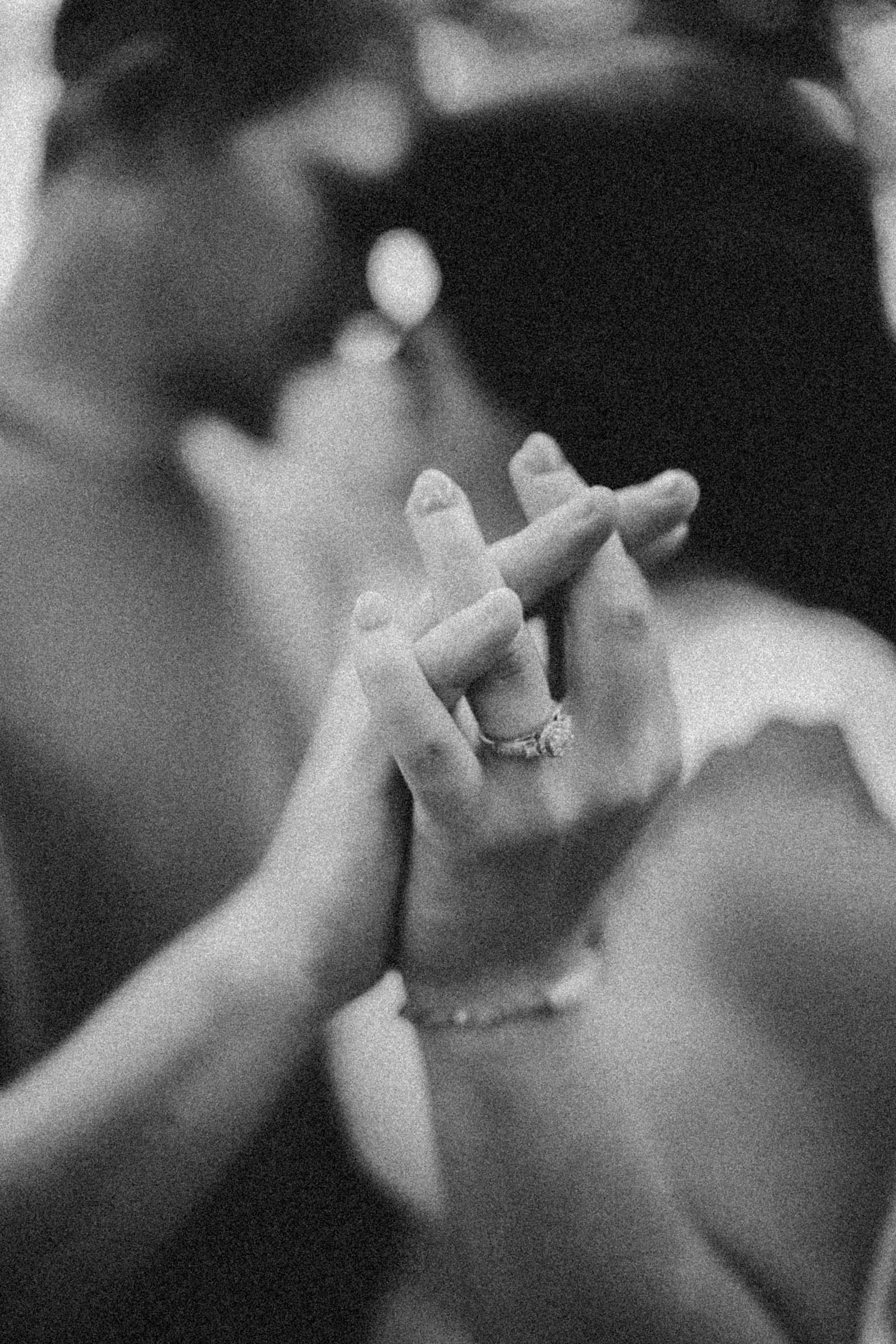 Black and white photo of couple holding hands, showcasing an engagement ring while sharing a romantic moment.