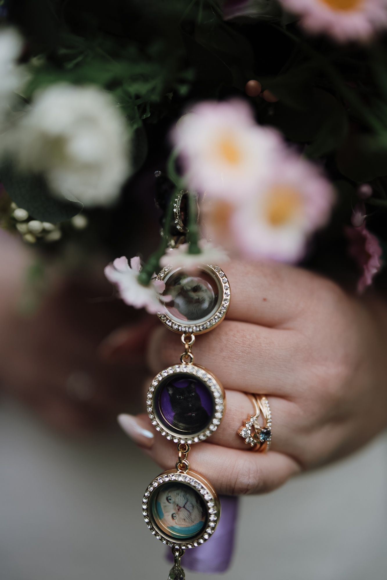 Close-up of a hand holding a floral bouquet with elegant locket charms and a diamond ring.