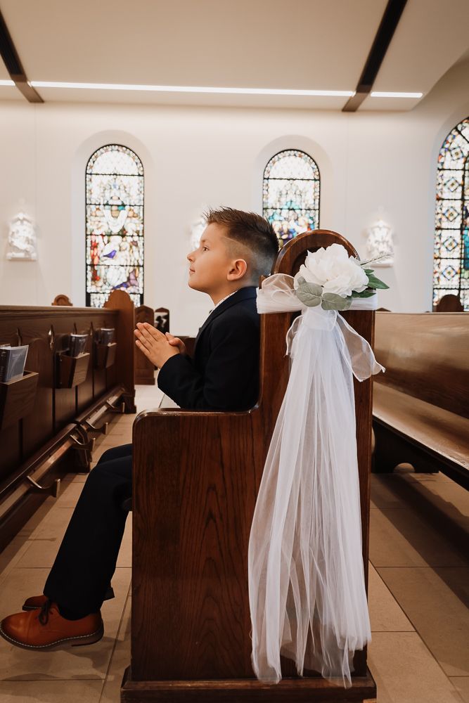 Boy in suit praying in church pew during First Communion, stained glass windows in background.