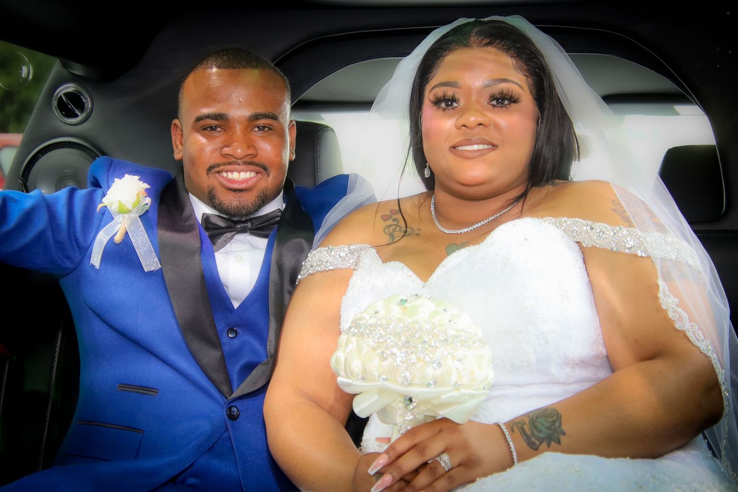 A couple in wedding attire sits together in a car sharing a joyful moment during their celebration.