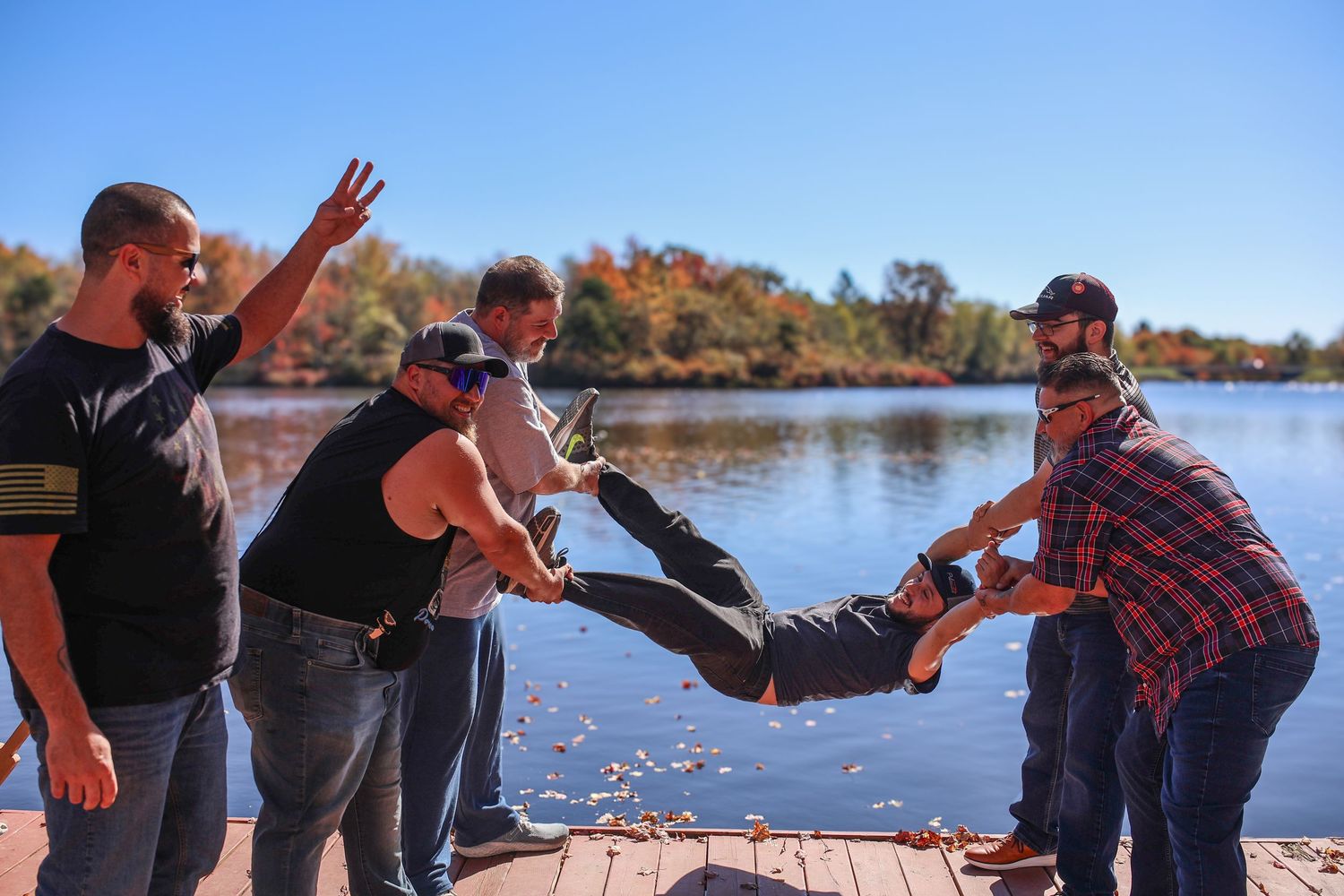 Group of friends toasting and celebrating with drinks by a scenic lake on a sunny autumn day.