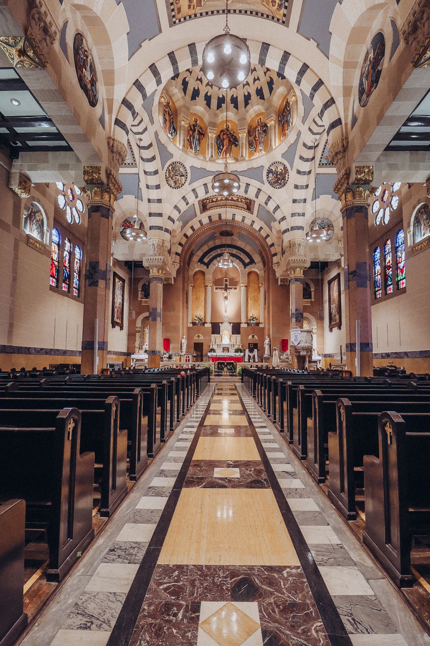 Interior view of ornate church sanctuary with arched ceilings, marble columns, and rows of wooden pews along center aisle.