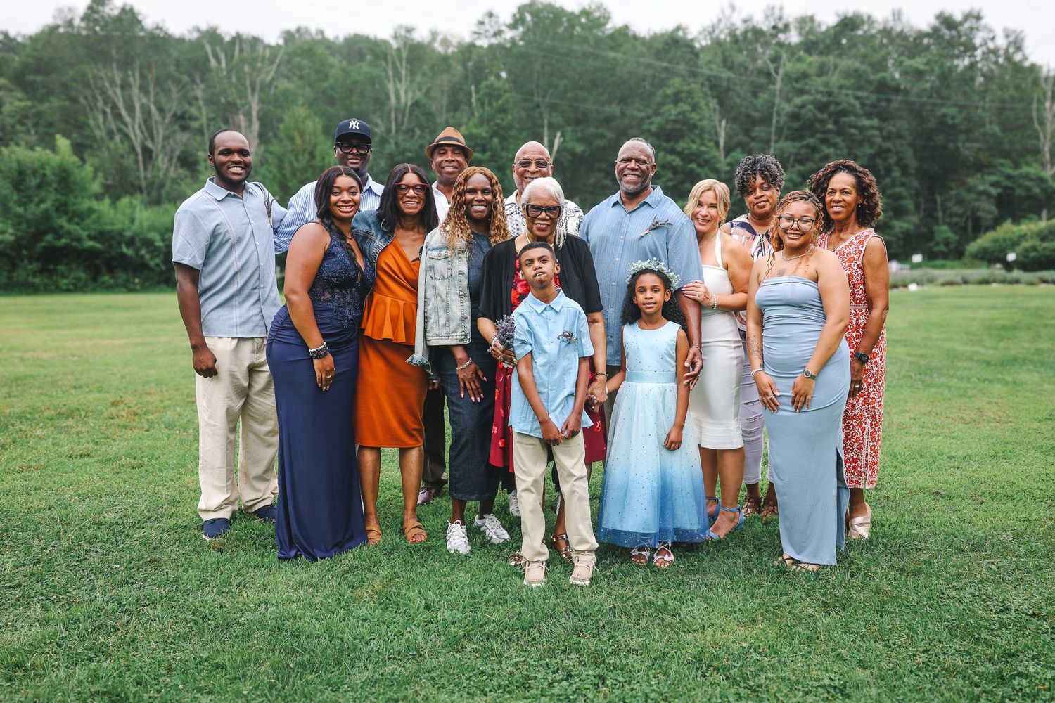 A group of people wearing coordinated orange and blue outfits pose together on a grassy field during a summer gathering.