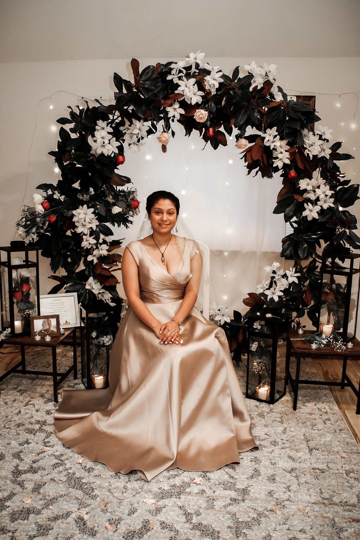 Elegant wedding setup with floral arch made of dark leaves and white flowers against twinkle lights and lantern decor.