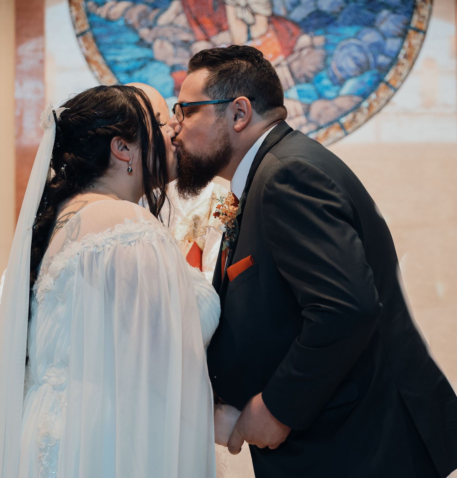 A tender moment between newlyweds sharing their first kiss during a wedding ceremony under a decorative circular backdrop.
