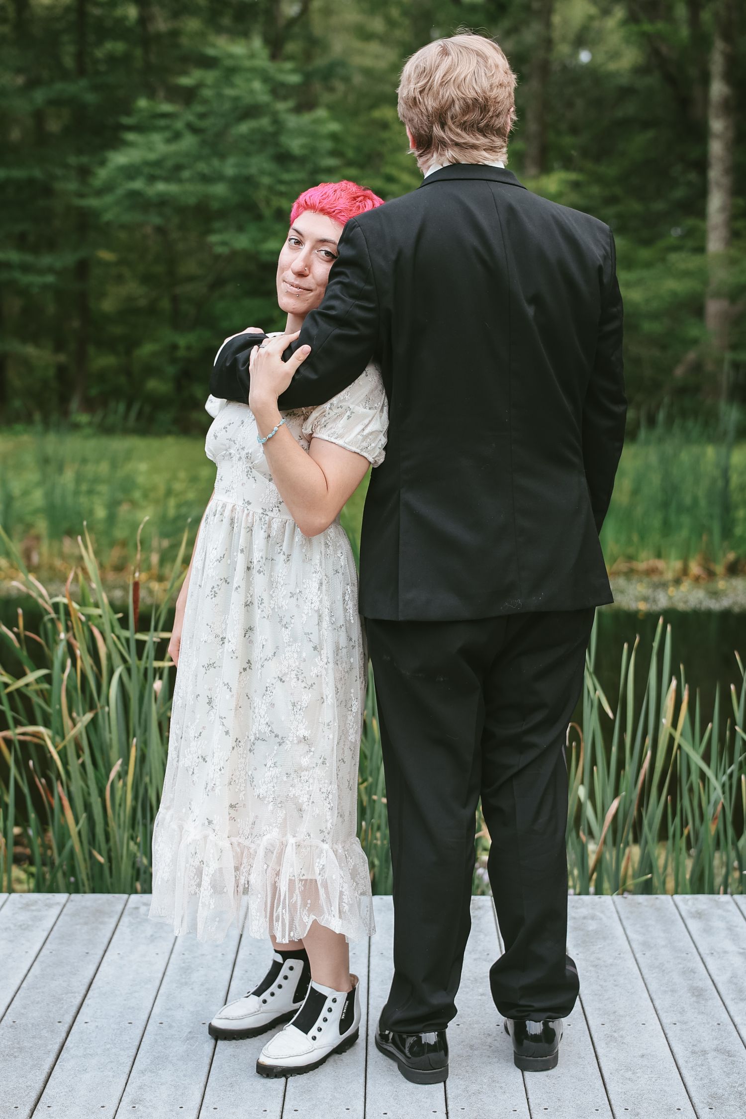 A couple stands on a wooden dock by a pond with cattails, shown in a series of playful peekaboo poses.