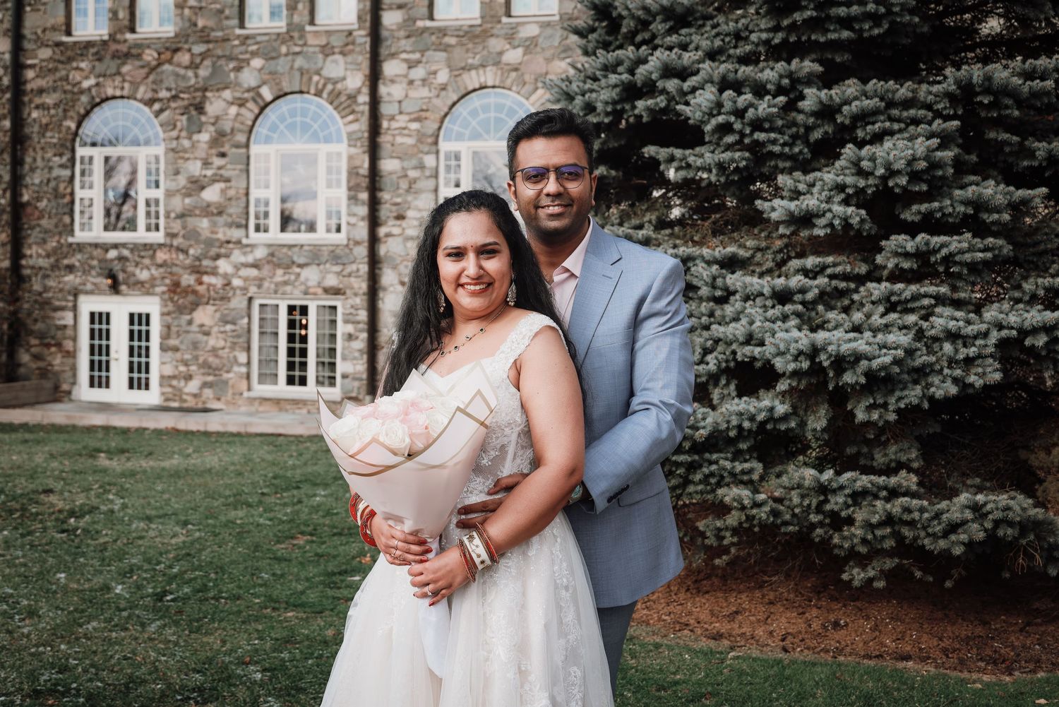 A couple shares an intimate moment outside a stone building during their wedding celebration.