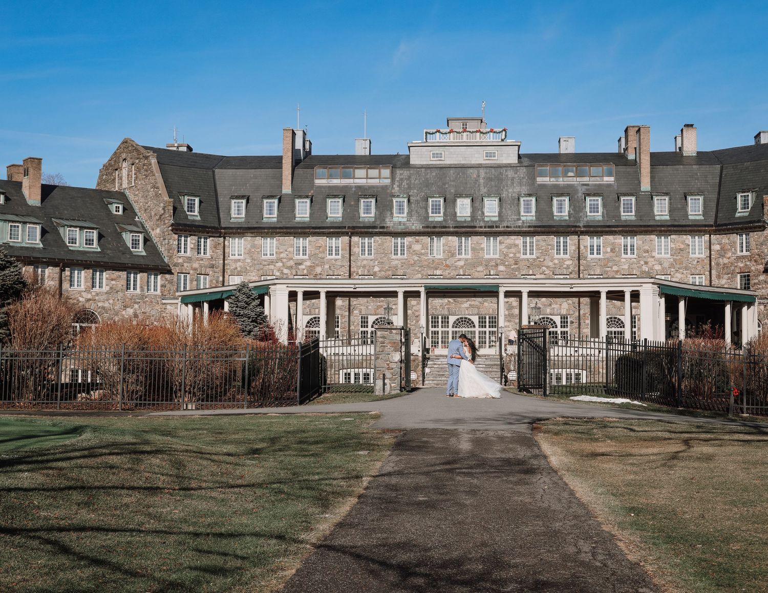 Historic mansion with columned entrance portico and symmetrical wings viewed across a formal lawn on a sunny day.