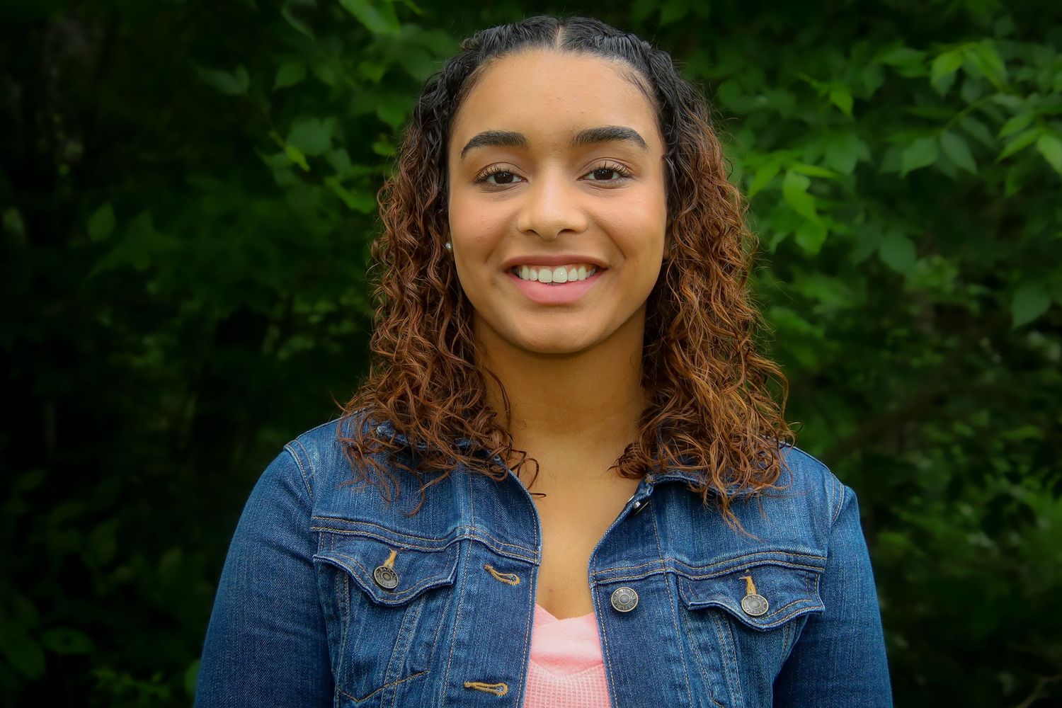 A series of headshots showing someone with curly hair wearing a denim jacket against a green leafy background.