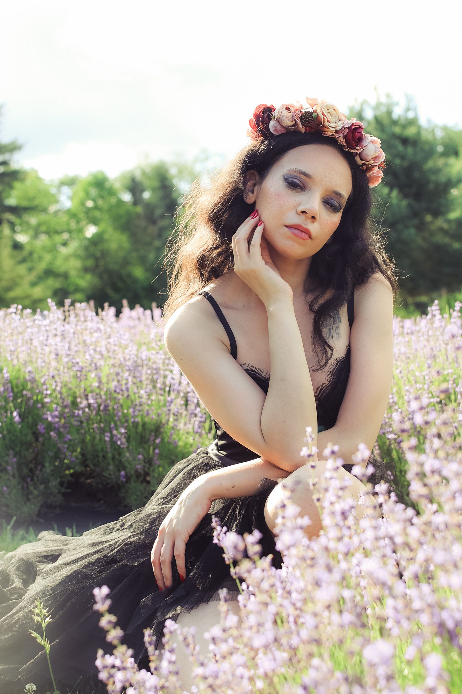 A dreamy portrait series in a lavender field shows a person wearing a black dress and floral crown at sunset.