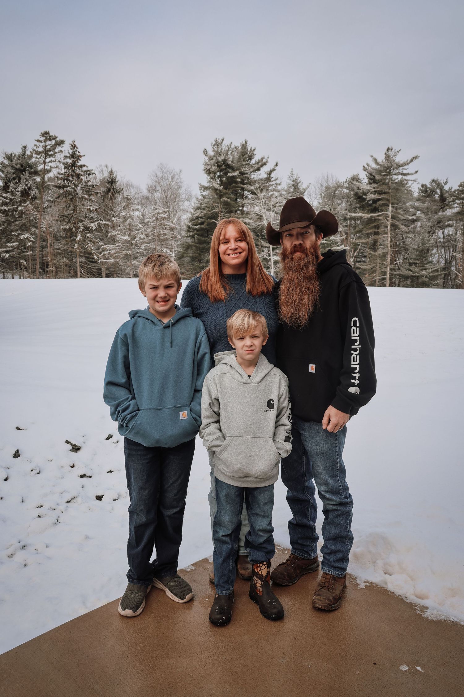 A family of four stands together in a snowy winter landscape wearing casual clothing and warm layers.