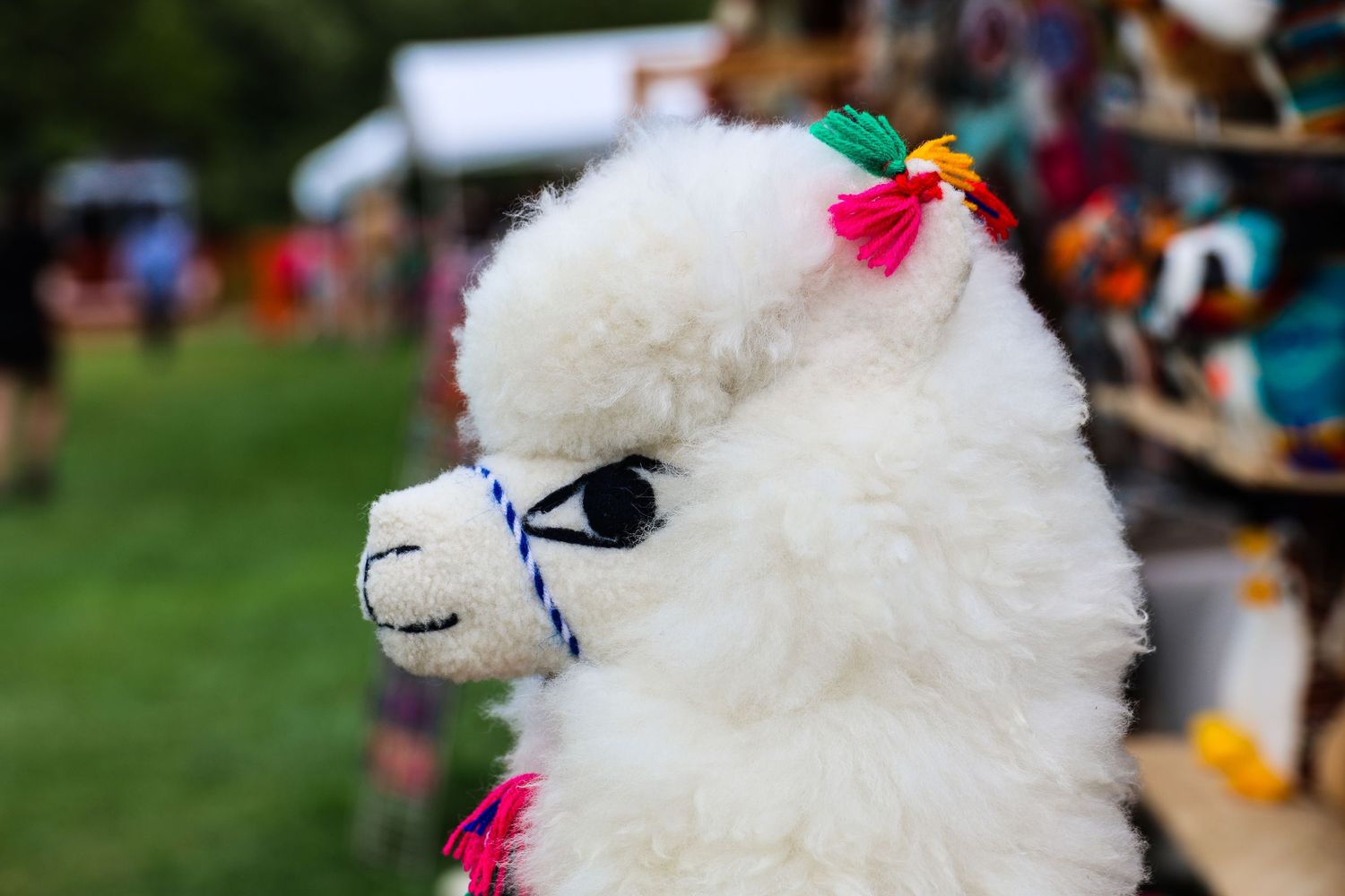 A row of white fluffy stuffed animals with pink bows on display at an outdoor market or festival.
