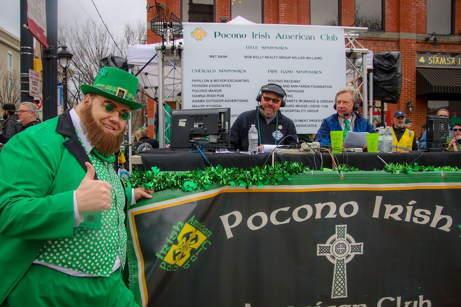 A person in bright green St. Patrick's Day attire poses with the Pocono Irish Club banner at a festive event.