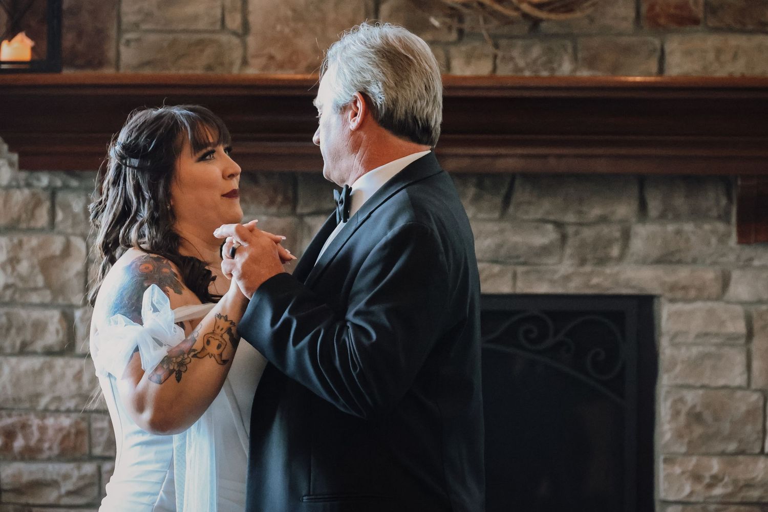 A bride and father share an emotional dance moment during a wedding reception in a rustic stone venue.