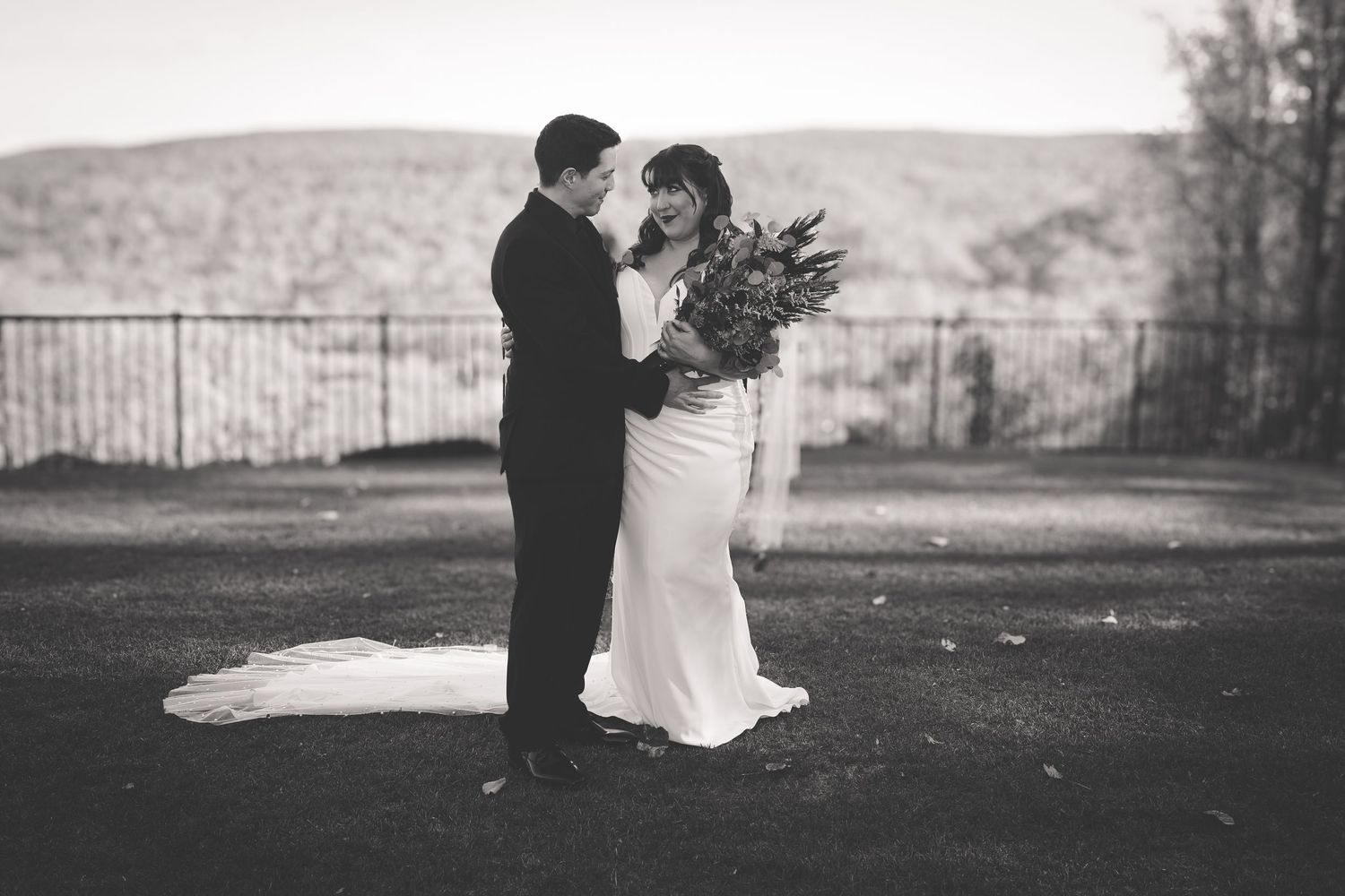 A black and white wedding photo shows a couple sharing an intimate moment outdoors with a bouquet of flowers.