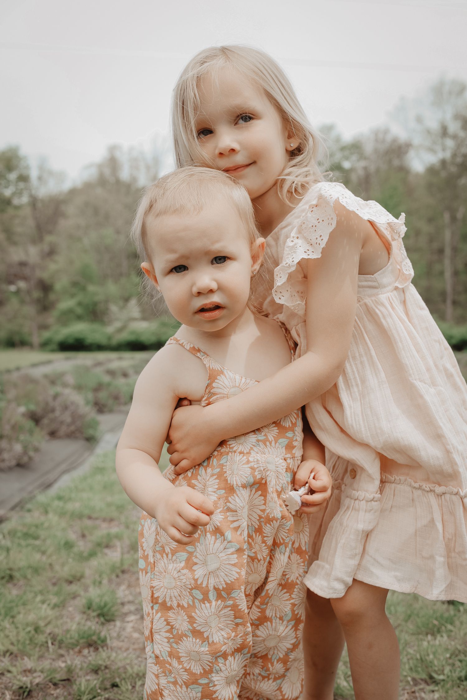 Sweet toddler in a delicate peach-colored dress plays in a natural outdoor setting during a sunny day.