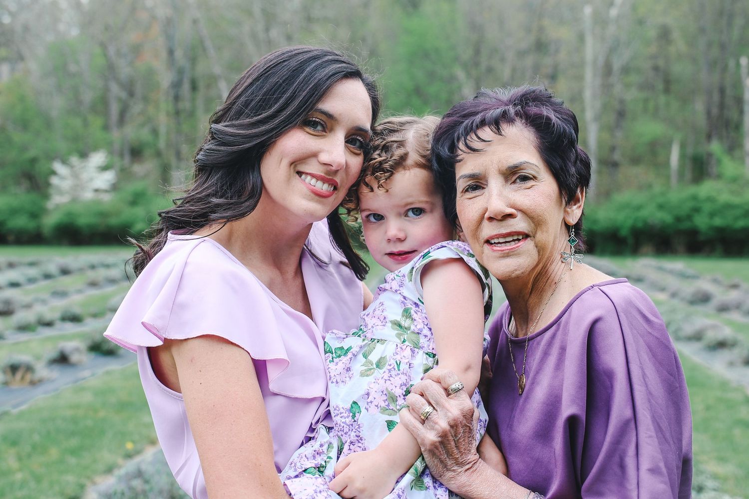 Three generations of family members share joyful moments together outdoors in coordinating pink and purple outfits.
