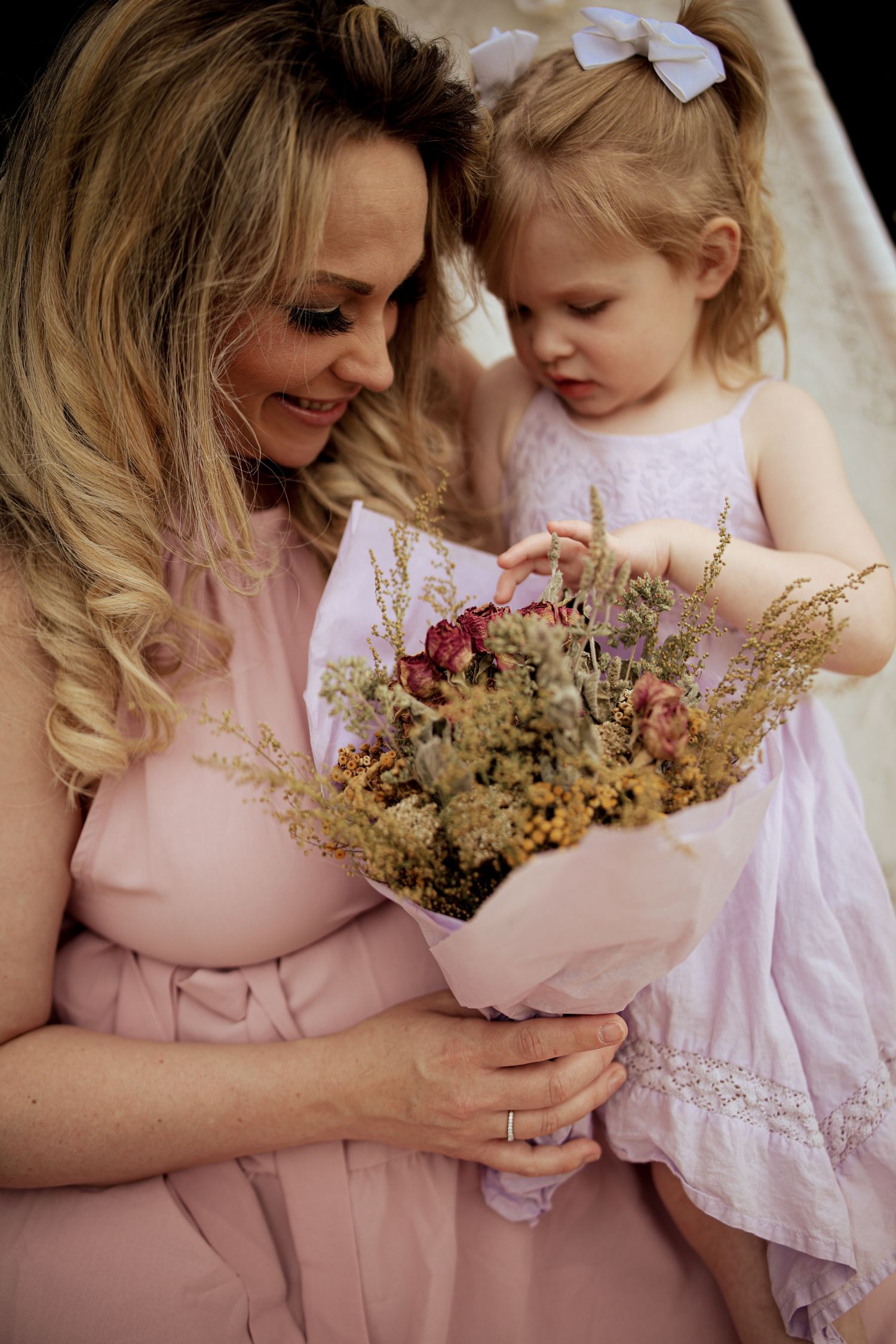 A tender moment between parent and child in matching pink outfits holding dried flowers and embracing.