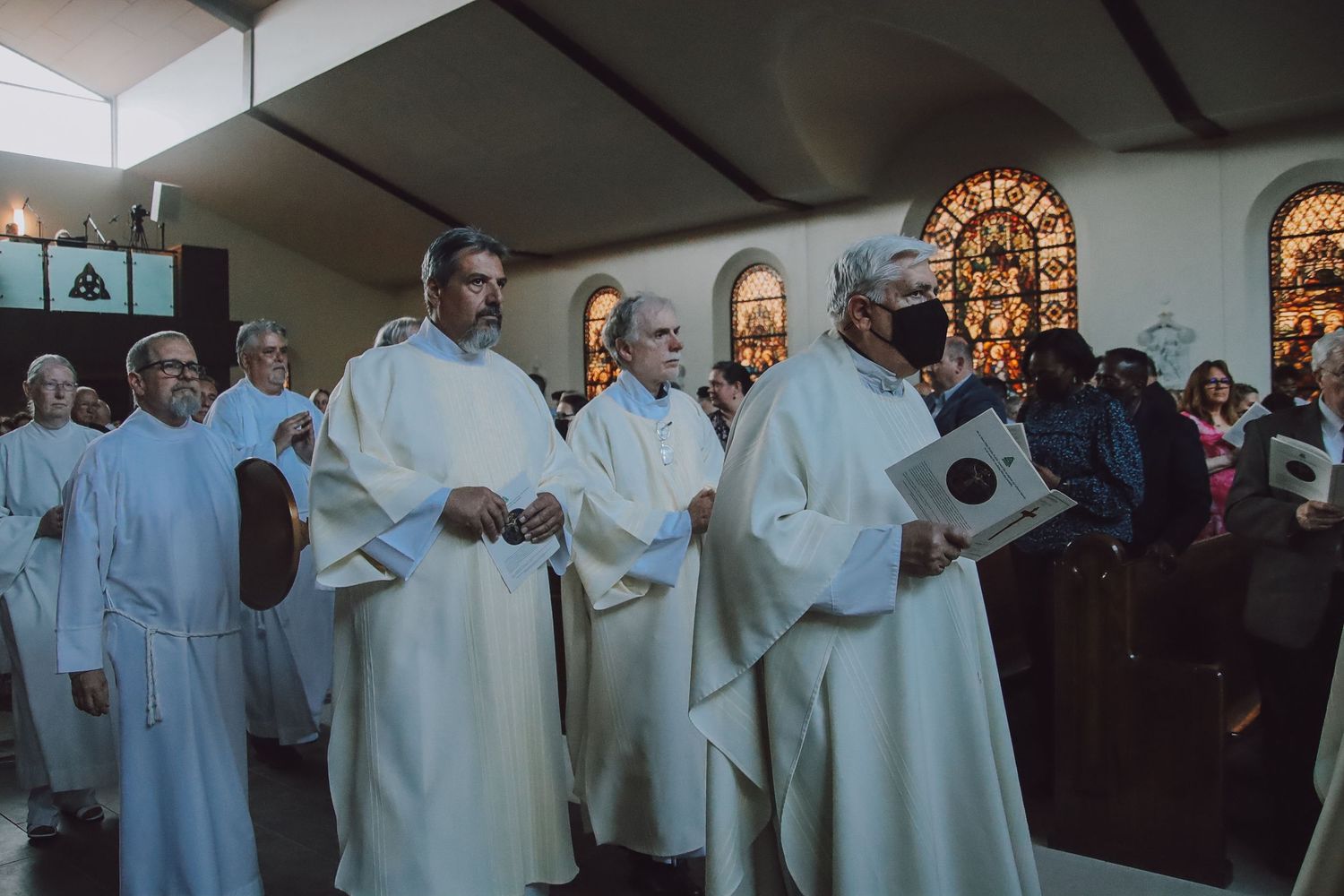 A group of clergy members in white robes participate in a religious ceremony inside a church.