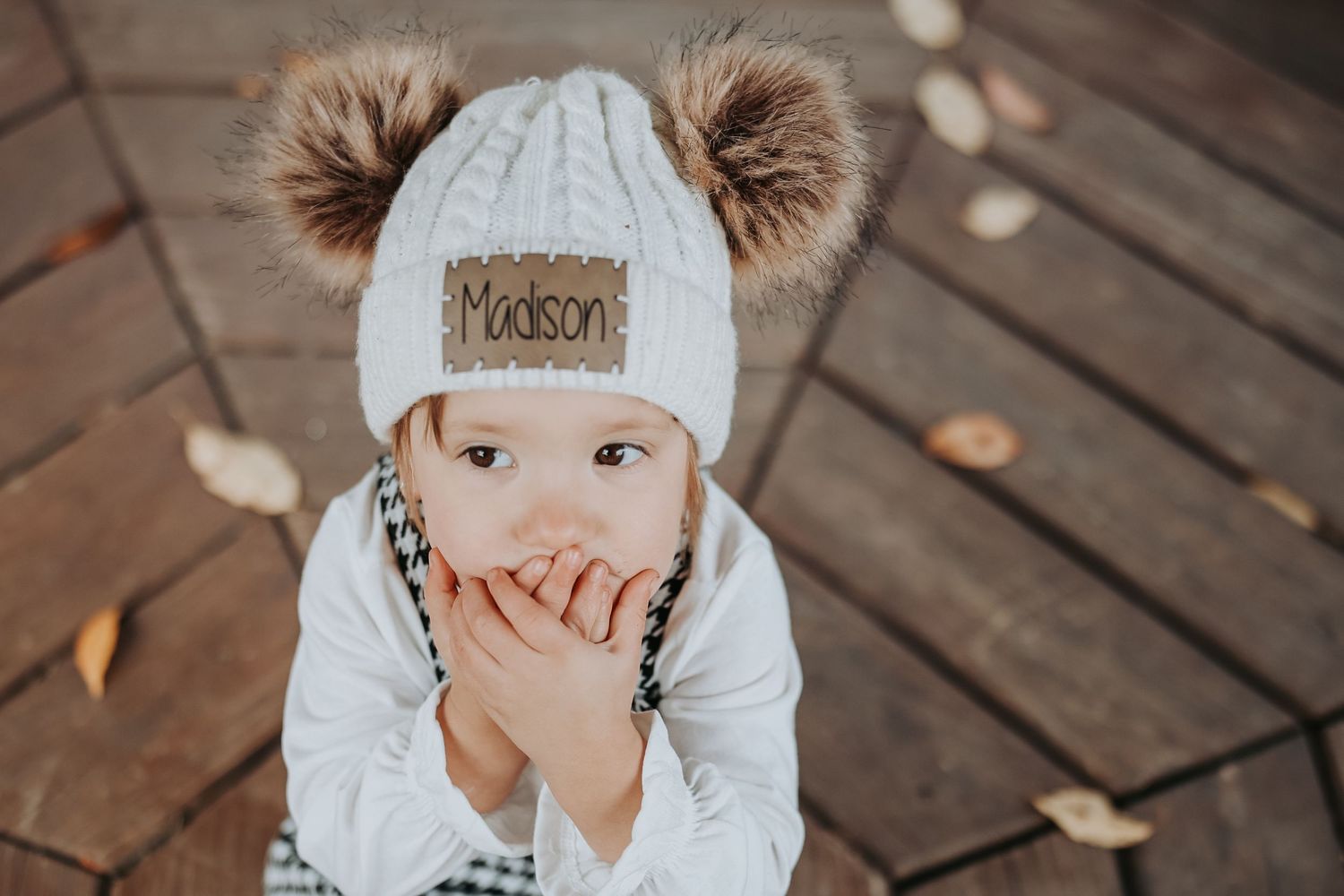 A series of candid moments showing a young child in a white beanie playing on wooden decking outdoors.